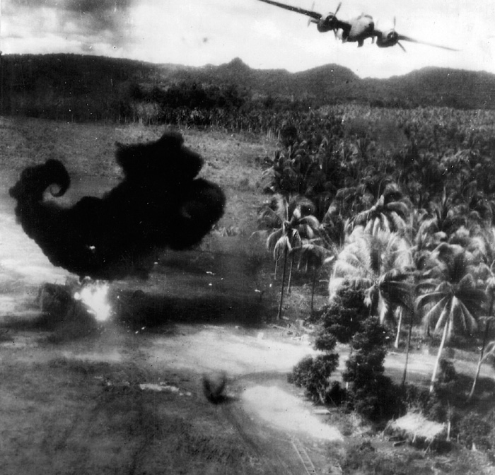 A B-25 bomber swoops low over a fiercely burning Japanese fighter in New Guinea. 