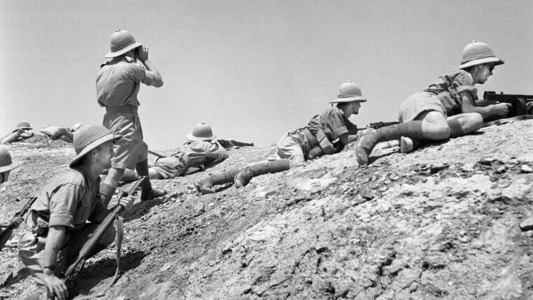 Wearing distinctive pith helmets, British soldiers assume prone positions as their commander scans the horizon for enemy activity. These troops were photographed near Ramadi, Iraq, as the British attempted to secure Middle Eastern oil reserves.