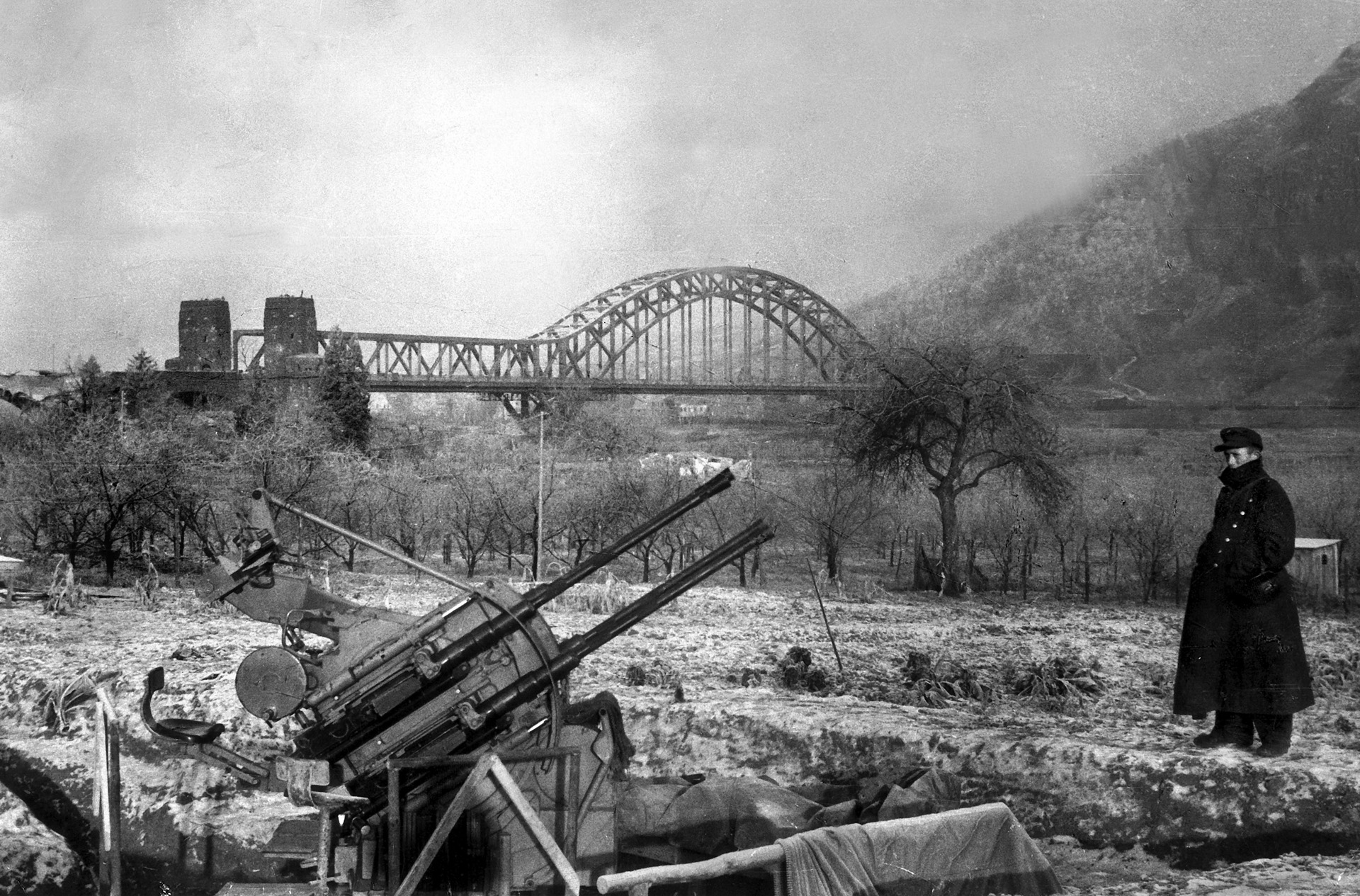 With the Ludendorff railroad bridge in the distance, a German soldier inspects an antiaircraft gun position on the east bank of the Rhine in January 1945. Weeks later, elements of the U.S. First Army were using the bridge to cross into Germany.