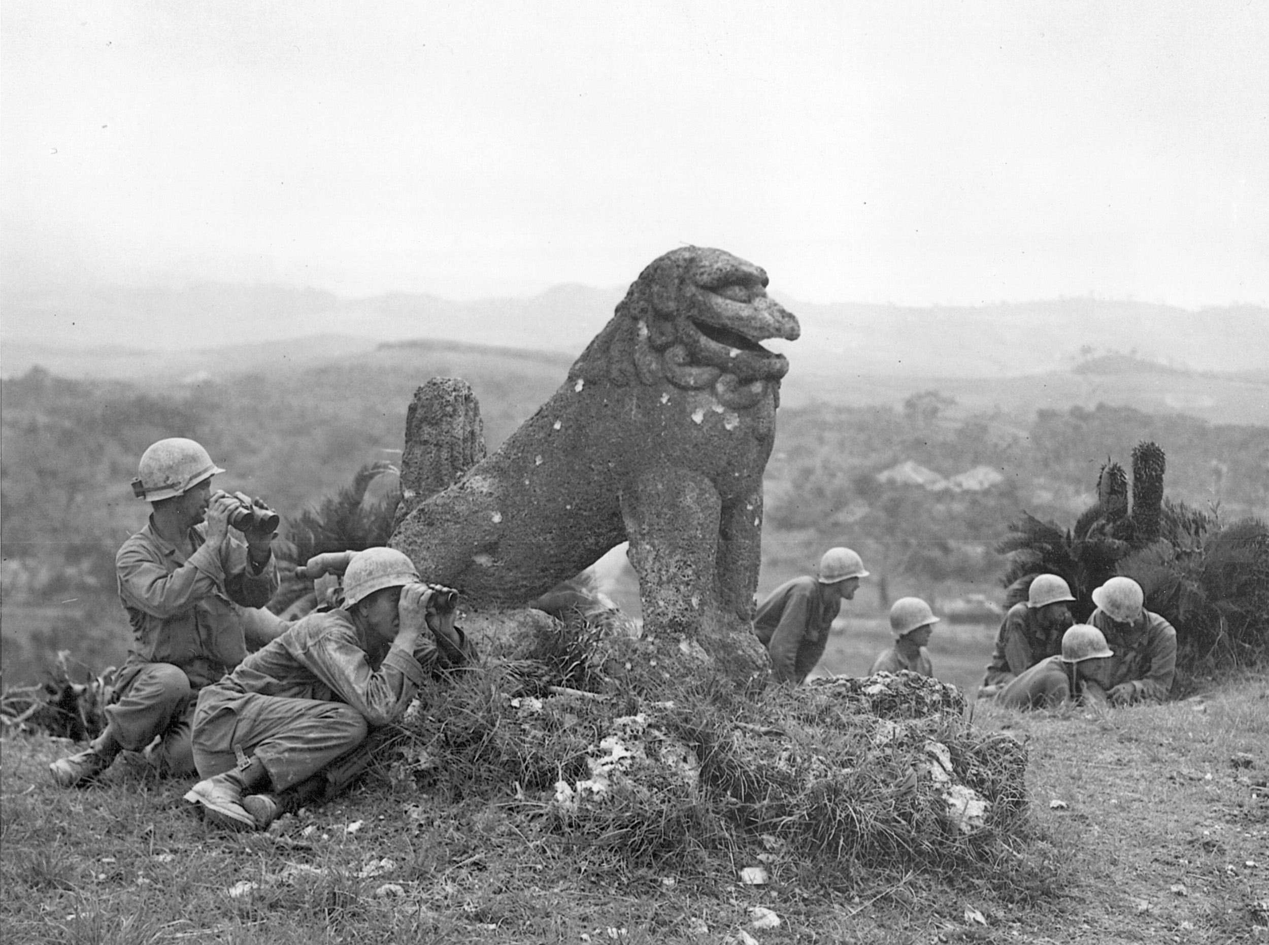A battered Okinawan statue shows the effects of recent shellfire while observers of the U.S. 7th Infantry Division use it as partial cover. Japanese mortar and artillery fire were often zeroed in on approaches to strongpoints. As a result, costly and time-consuming assaults were required to complete the capture of the island.