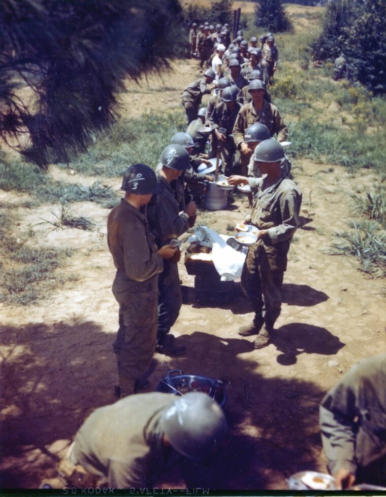 Chow time in the chow line. Their helmets chalked with class numbers, these trainees work their way through a chow line at Fort McClellen, Alabama. 