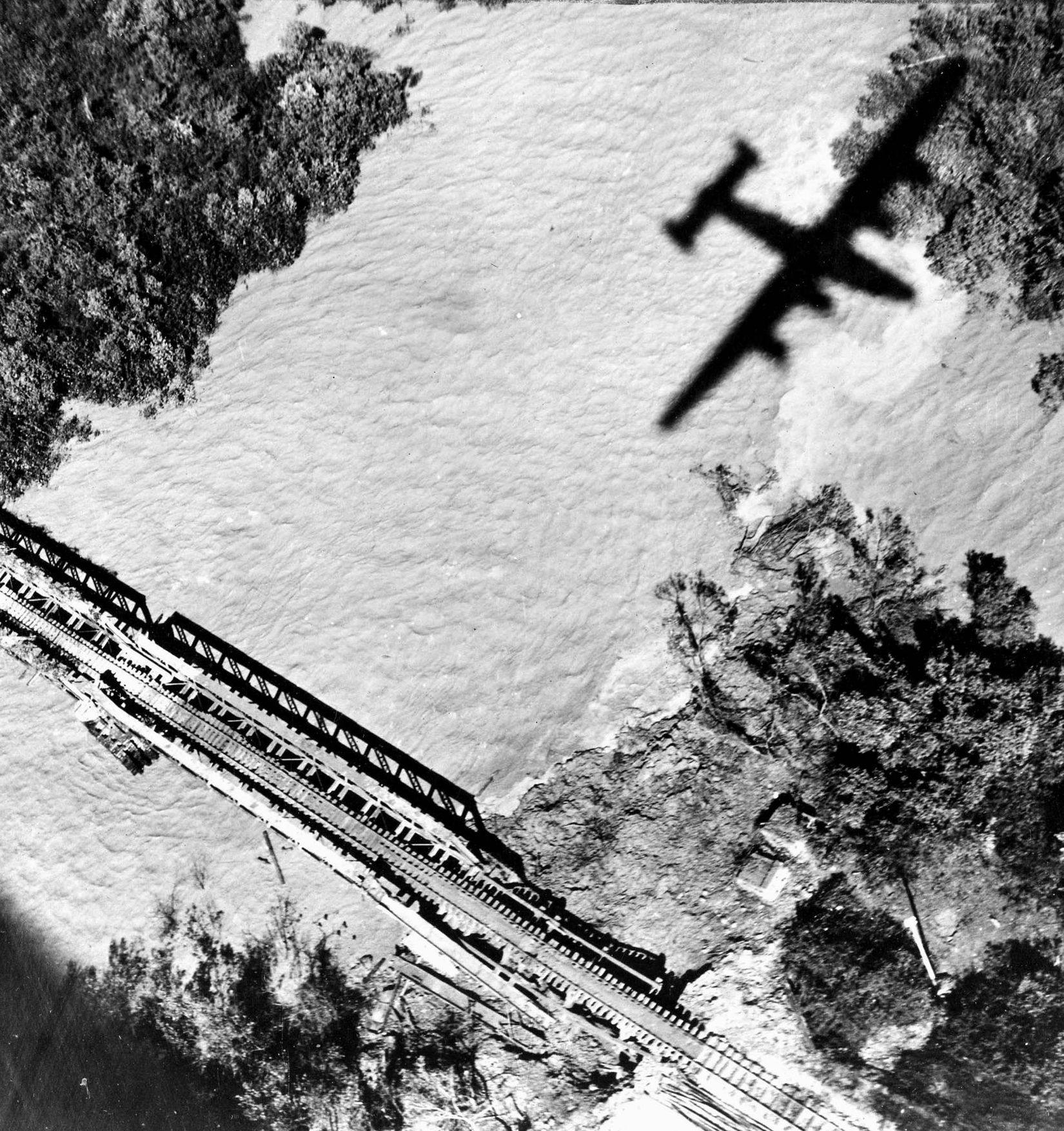 An American B-24 from the 7th Bombardment Group literally shadows a Japanese railroad bridge at Moulmein-Ye in January 1945. The bridge was one of three transporting enemy supplies to Burma.
