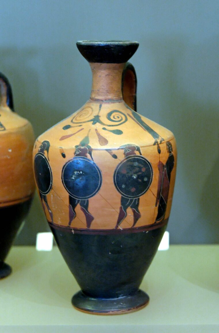 Greek hoplites, shields in hand, march colorfully around this terra cotta vase. The real invasion was not as simple.