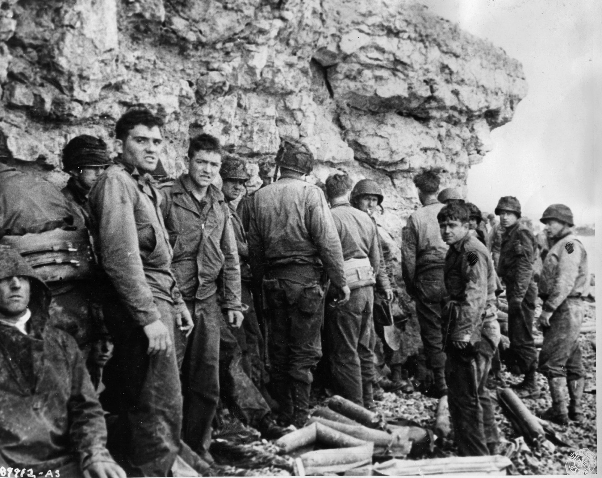 After hours of harrowing combat and finally gaining the upper hand at Omaha Beach, these soldiers of the 16th Regiment, 1st Infantry Division rest in the shelter of the steep cliffs at Omaha Beach. This photo was taken in the vicinity of the French seaside village of Colleville-sur-Mer.