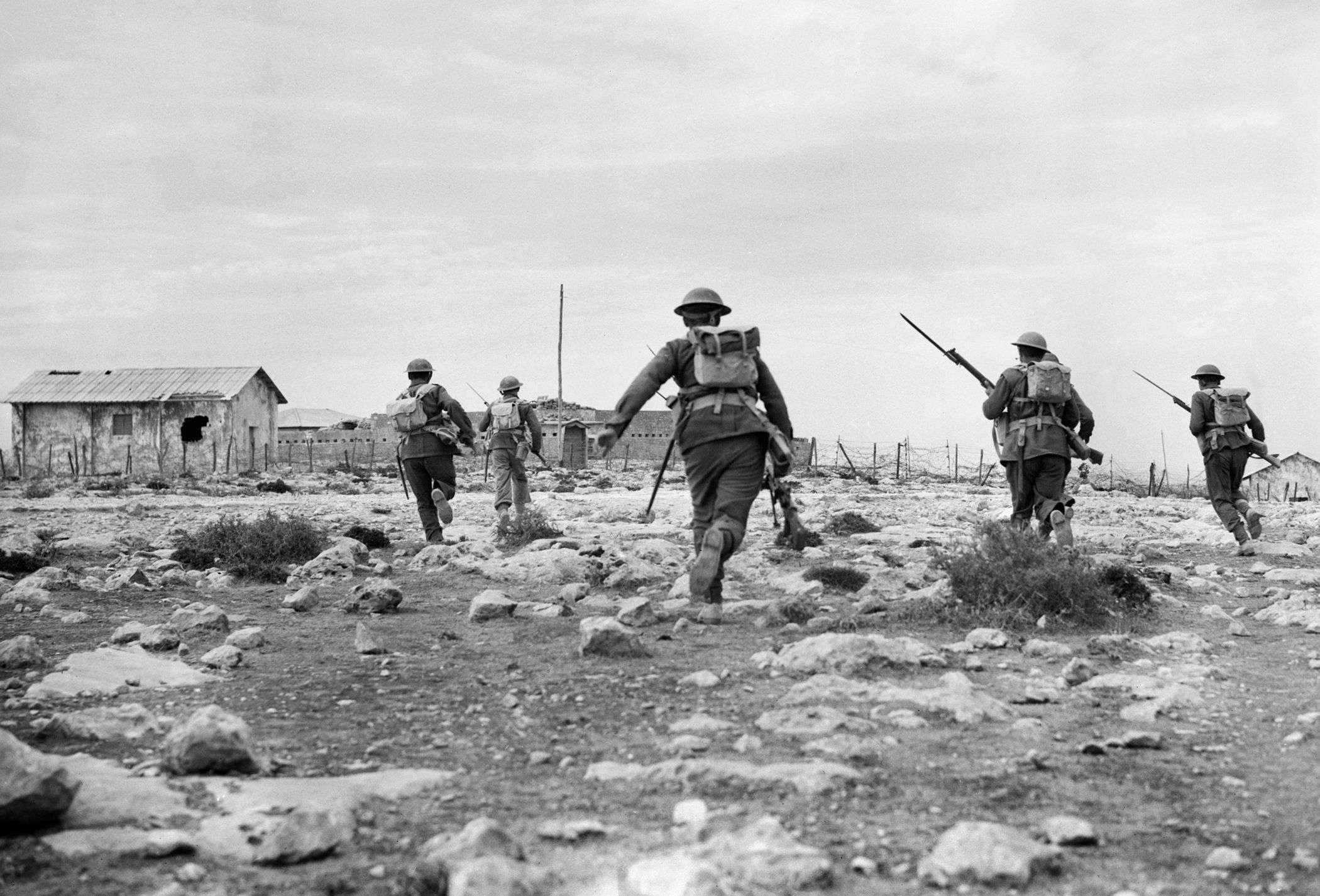 British soldiers advance rapidly toward barbed-wire entanglements in front of Italian fortifications at Derna on February 1, 1941. One of the British solders appears to be carrying a Bren gun, the standard issue infantry support machine gun of World War II.