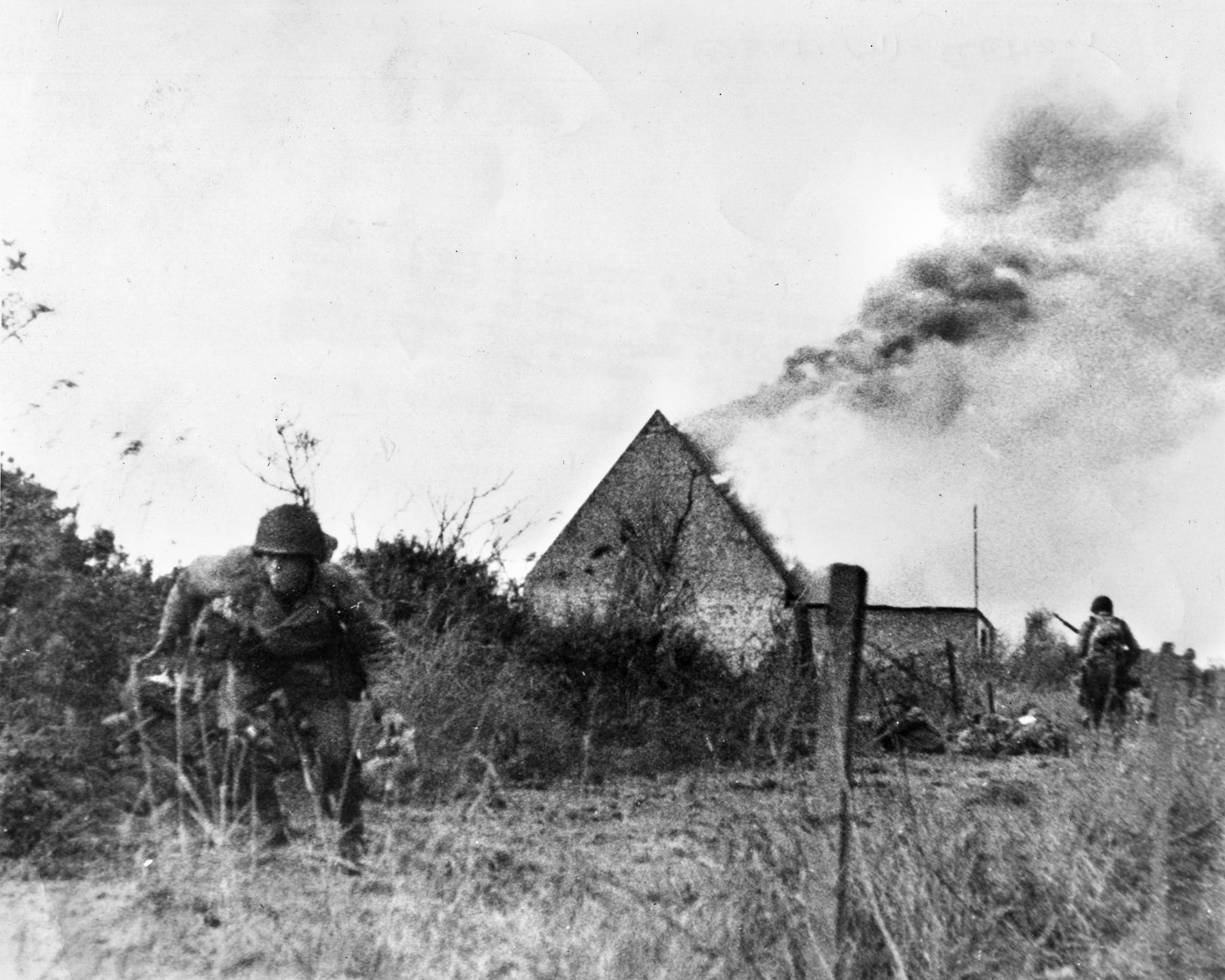 American soldiers scramble away from a burning house in Normandy. Mauser fired into a similar house filled with Germans in Vierville.
