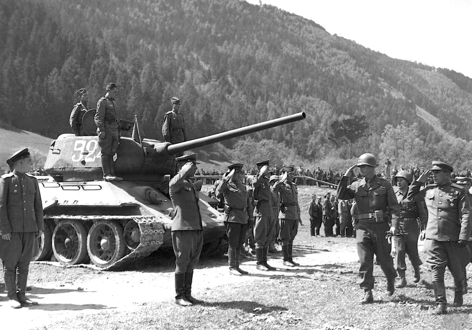 A detachment of Red Army Guards snaps to attention as a group of visiting Americans passes. A T-34 tank squats with the Soviets on a parade ground after the end of hostilities.