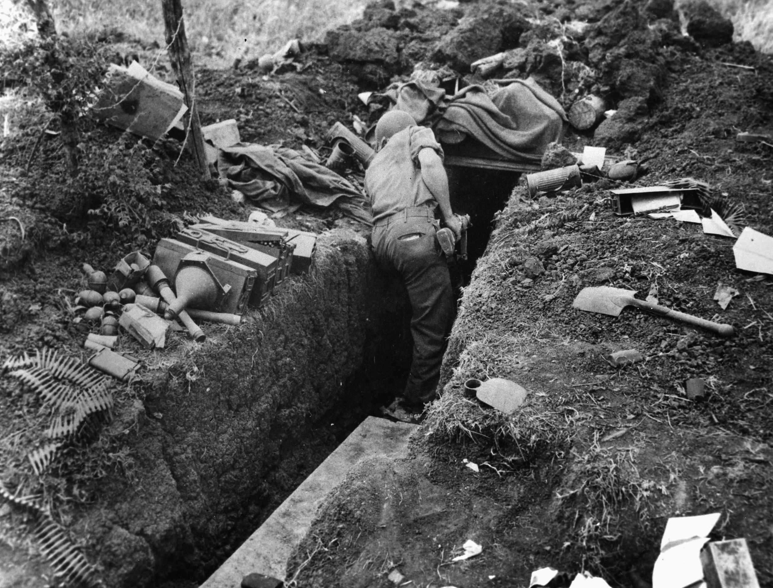 A GI cautiously examines a German trench along the Cisterna-Cori highway. Enemy ordnance lies scattered on either side. 
