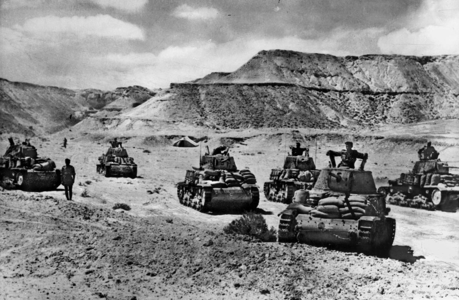 Italian tanks, carrying sandbags for better traction and protection, advance through a depression along the El Alamein line. The depressions—which featured escarpments and fine powdered sand—were difficult for armor to traverse.