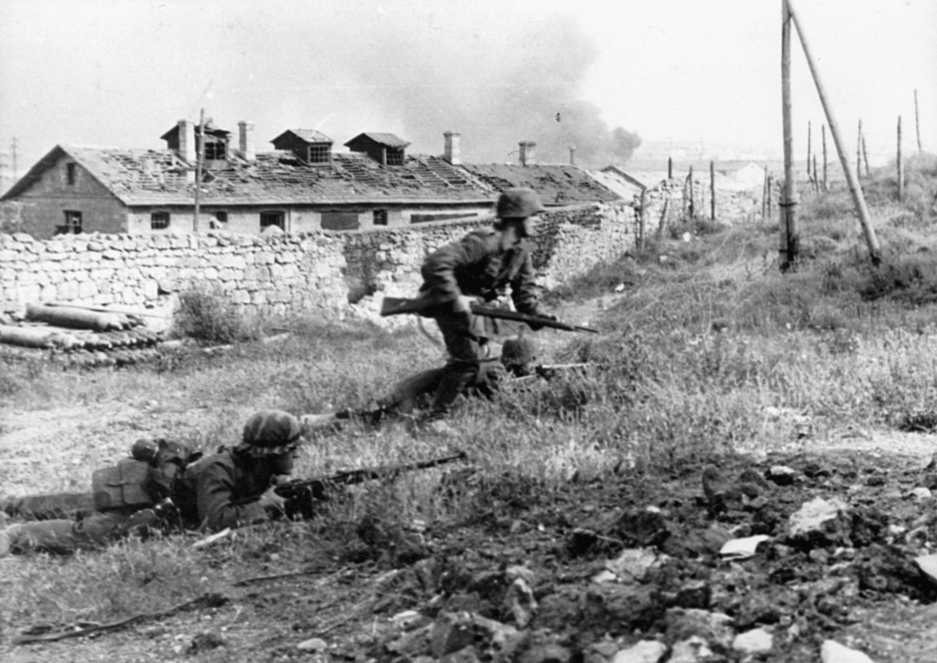 A German soldier exposes himself to Soviet gunfire as he attempts to push forward. His comrades continue to lie low behind the limited cover of a small embankment.