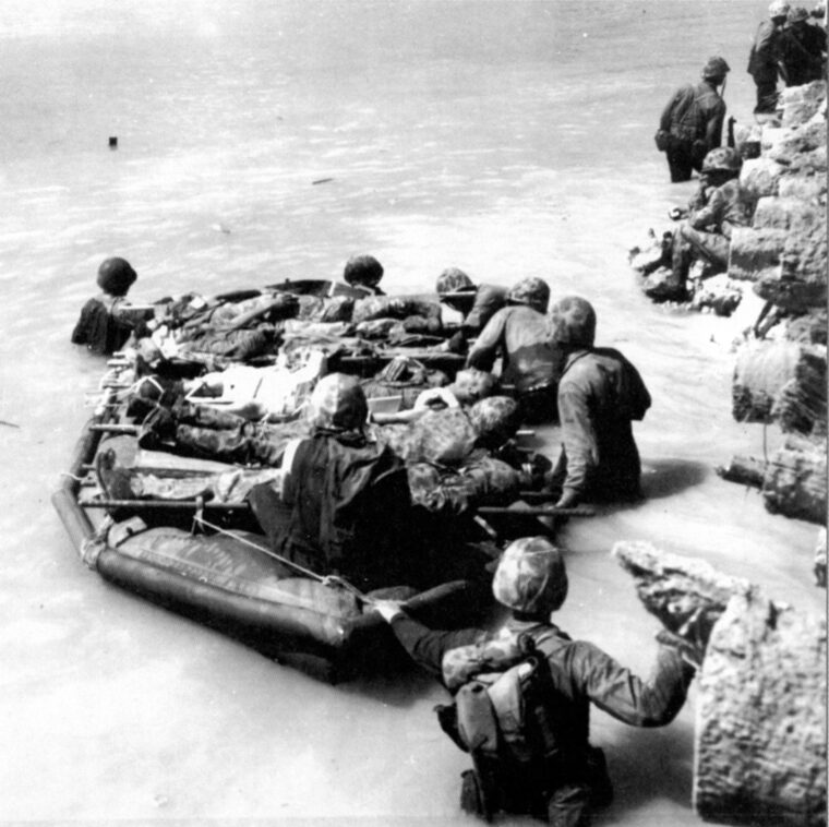 Wounded Marines lie on an assault raft while being ferried along a pier to waiting landing craft. Due to the difficulties of getting wounded men to safety in a timely manner, many died before they could receive comprehensive treatment.