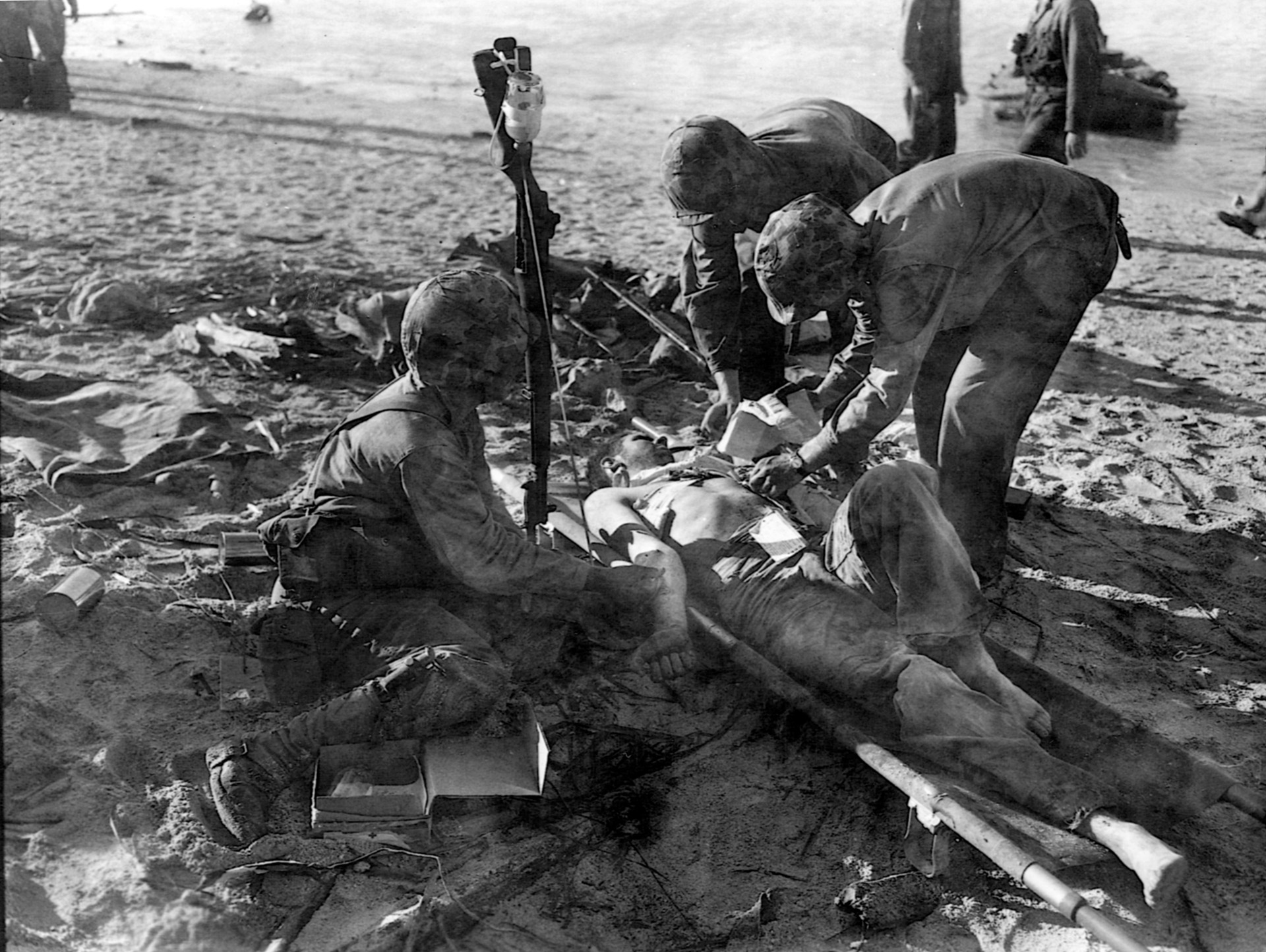 With a bottle of blood plasma positioned on the butt of an upended rifle, a Marine receives a lifesaving blood transfusion on the beach at Tarawa.