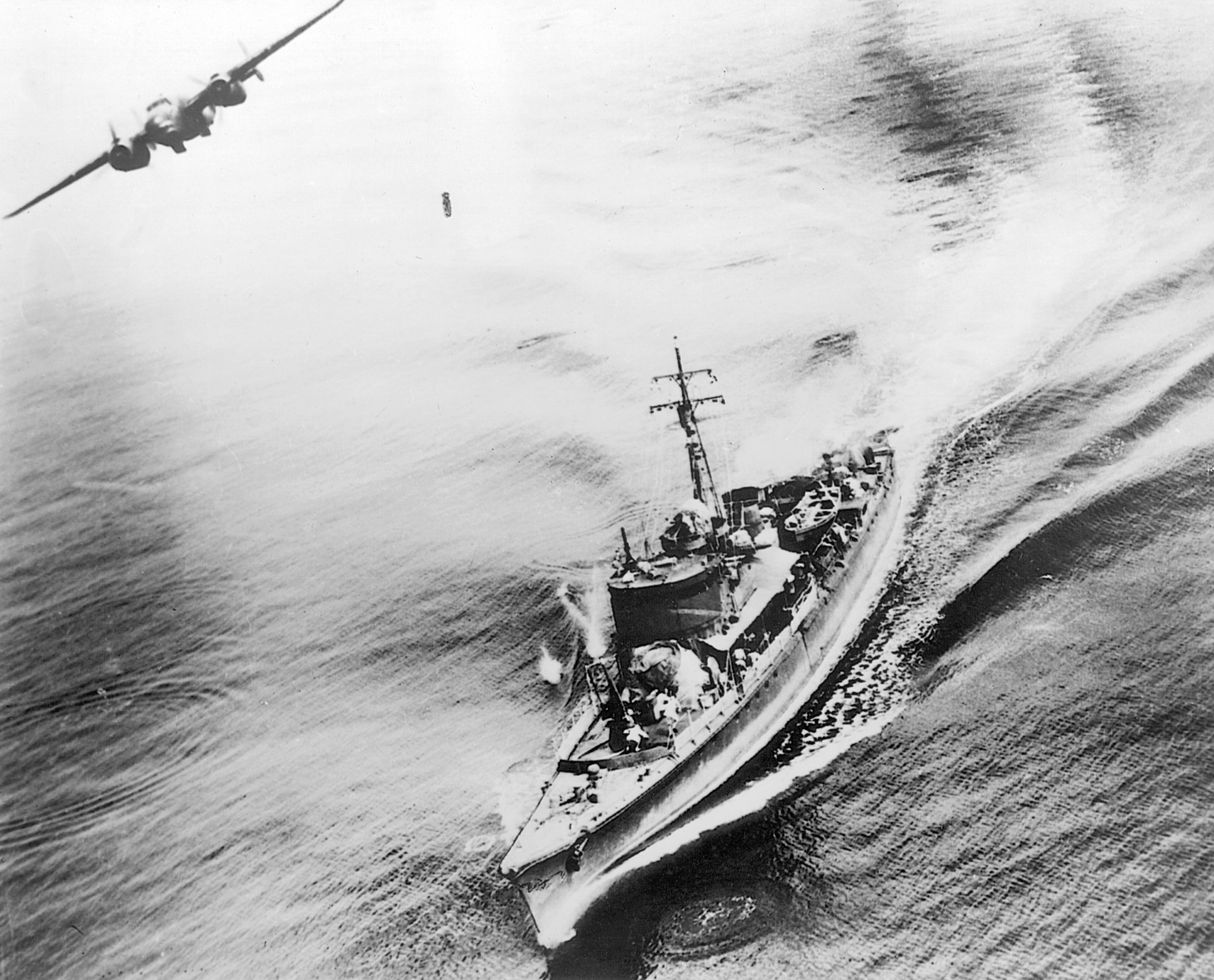 An American bomber banks away from a Japanese warship in the Bismarck Sea. Its bomb can be seen plummeting toward the pagoda-masted target below. 