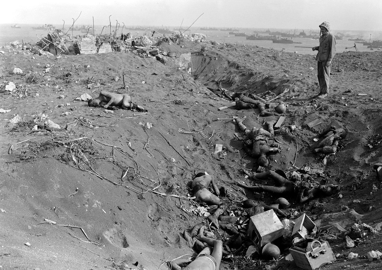 A Marine grimly inspects dead Japanese soldiers, their uniforms burned off when they were blasted out of a pillbox at Iwo Jima.