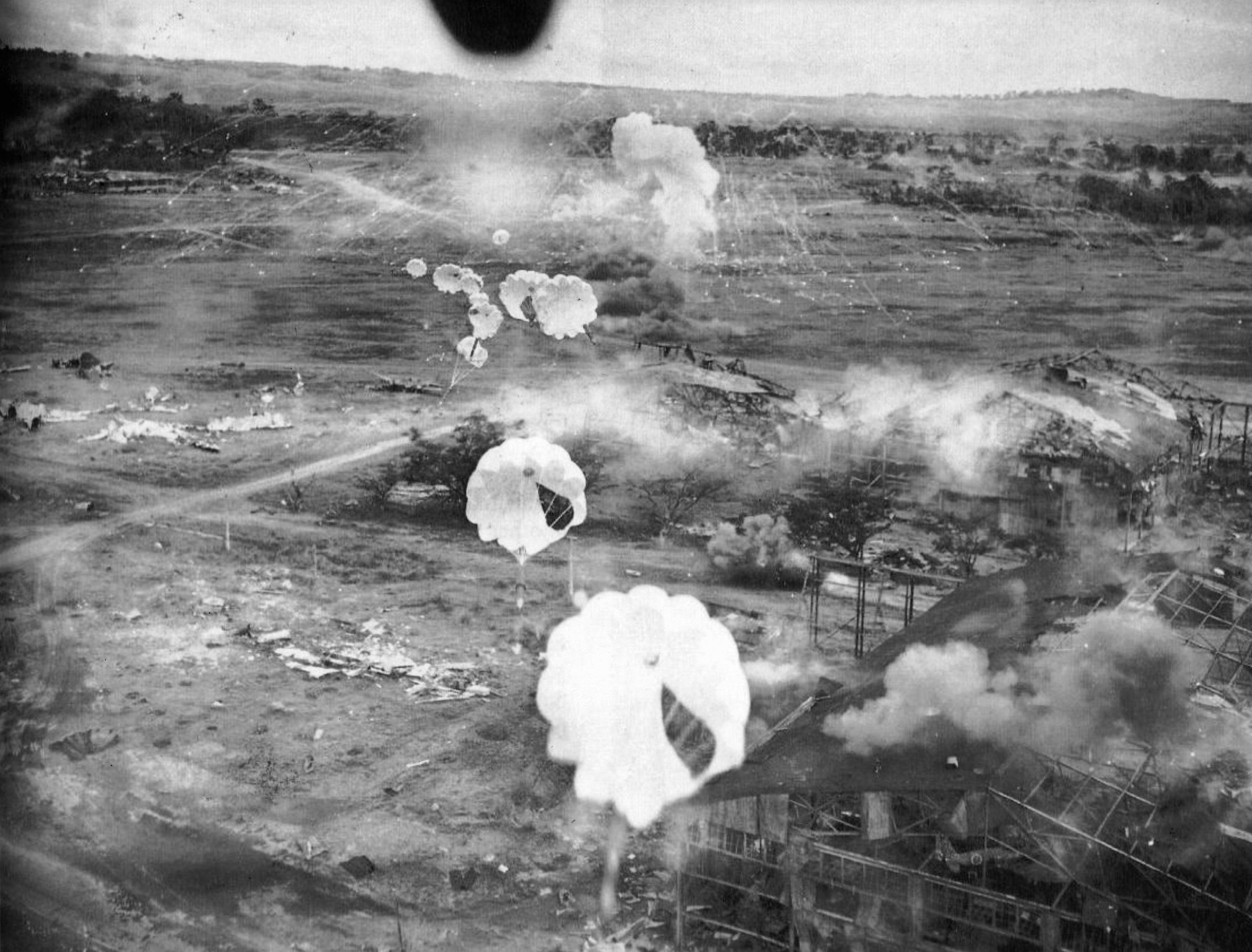 Lieutenant John T. Cooper flies his bomber low over the wreckage of the main hangar complex at Clark Field. The facility has sustained heavy damage, and smoke rises from a phosphorous bomb dropped among Japanese aircraft earlier in the raid. 