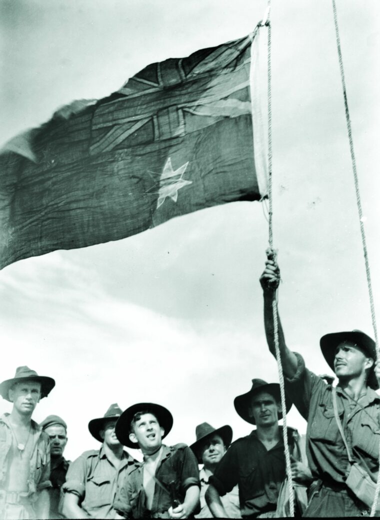Lieutenant K. McKitrick hoists the Australian flag on Sadau Island, Borneo, April 30, 1945.  The battle hardened soldiers of the 2/4 Commando Squadron look on during the impromptu ceremony.