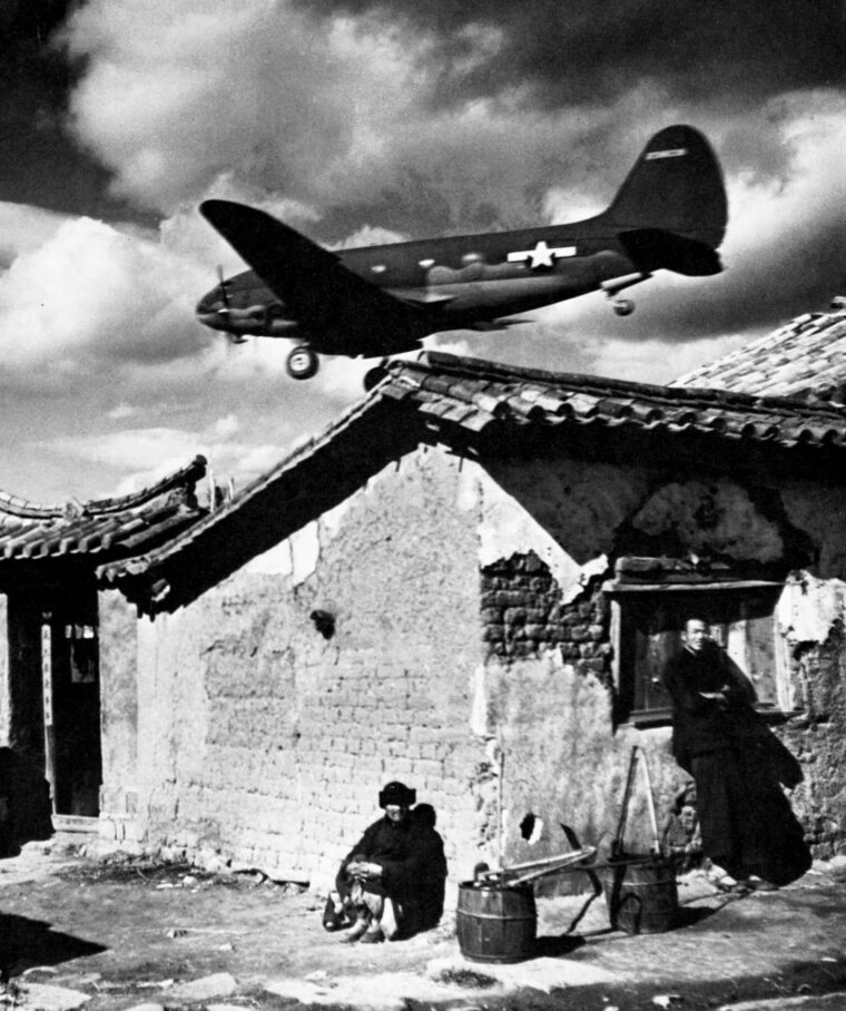 Coming in for a landing on an airfield near Kunming, China, a C-46 Commando transport plane flies low over the tile roofs of the nearby village.