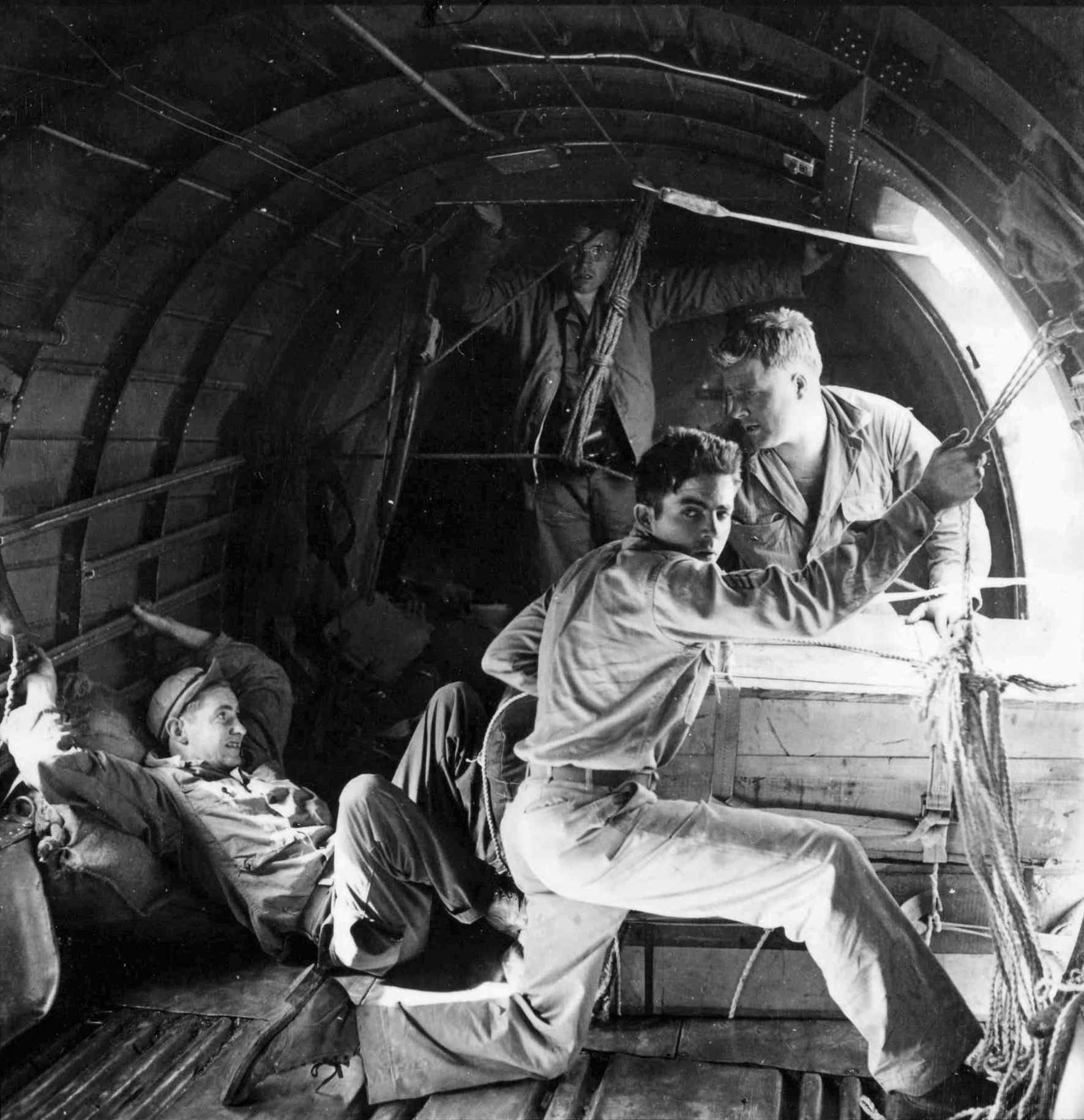 During the April 16, 1944, flight, Sergeant Donald Ross watches for a signal from the cockpit of a C-47. Private Robert Crane is positioned against the side of a box, ready to shove it out the door. Pfc. Charles Banks is positioned behind the box, while Brig. Gen. Frank Merrill observes.