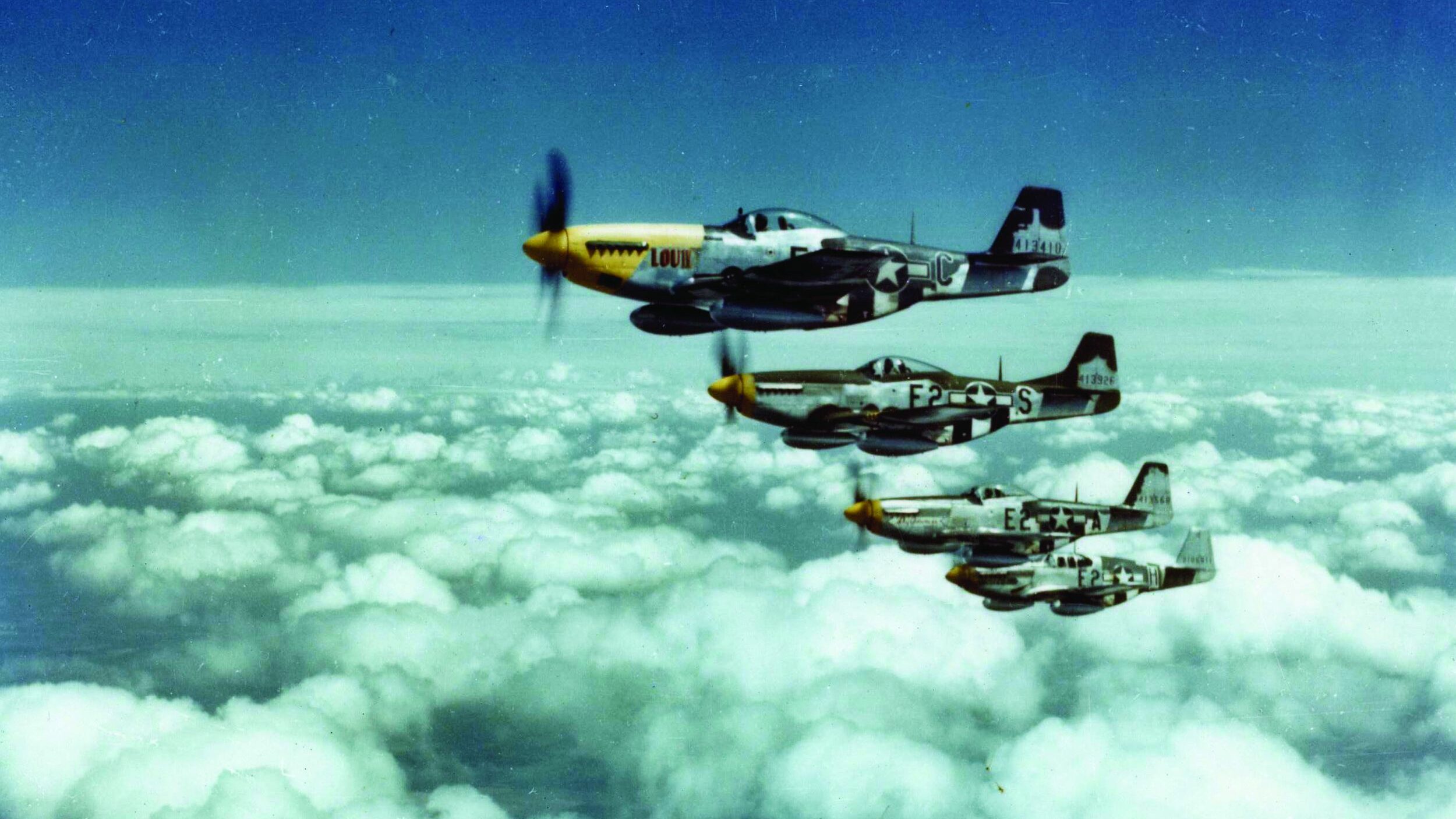 A flight of famed North American P-51 Mustang fighters flies in tight formation.