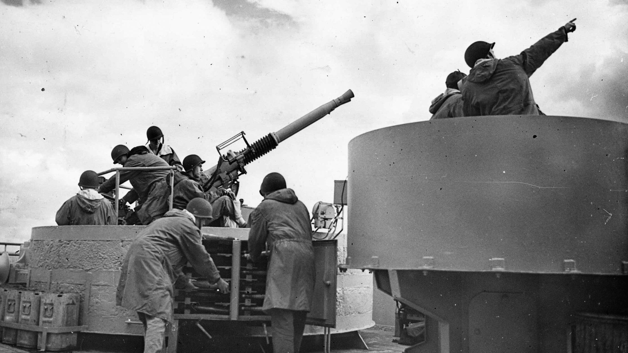 Manning a twin Bofors antiaircraft gun on the deck of the Queen Mary, a crew is put through its paces by an officer during gunnery training at sea.