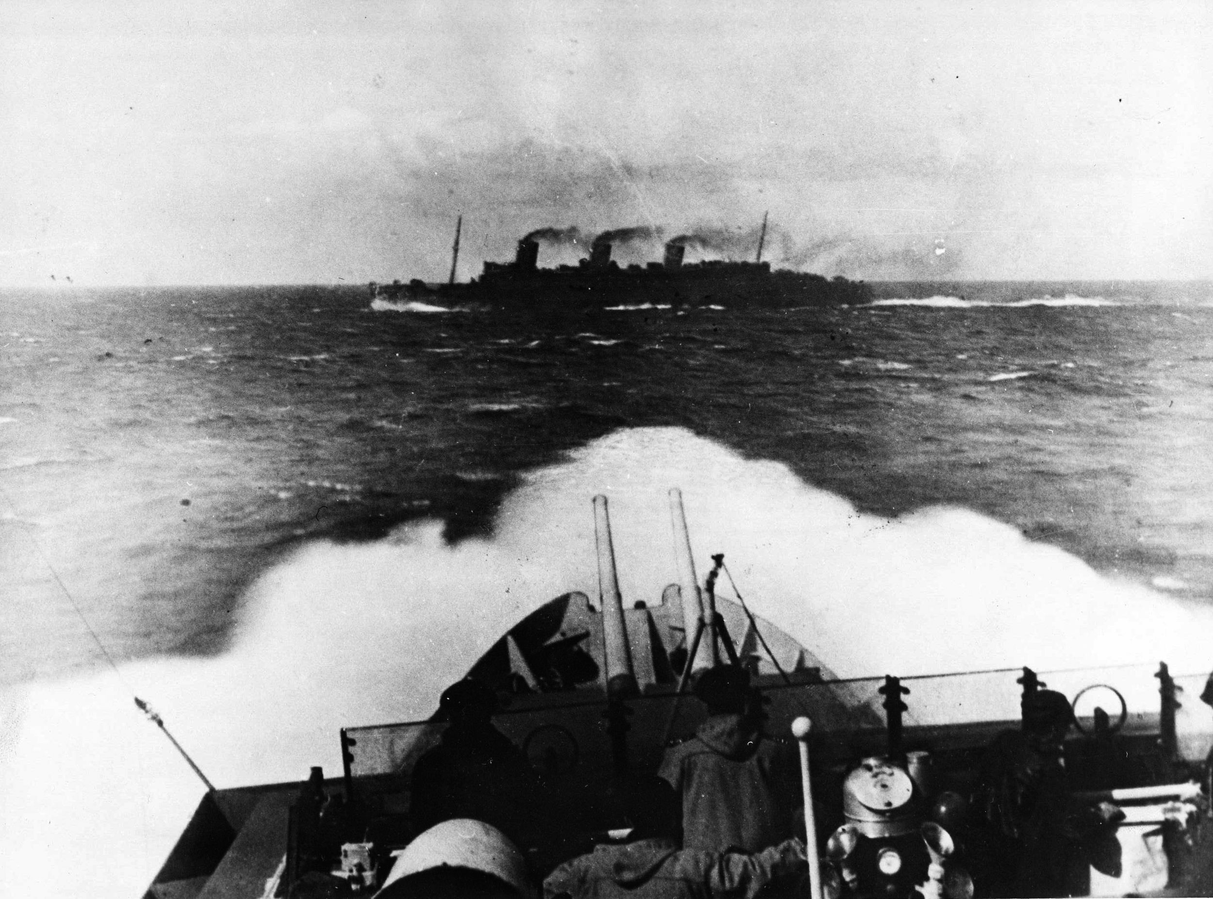 Seen from the bridge of the escorting British cruiser HMS Scylla, the Queen Mary slices through the waters of the Atlantic. During an unfortunate accident, the great liner collided with a Royal Navy warship, which quickly sank.