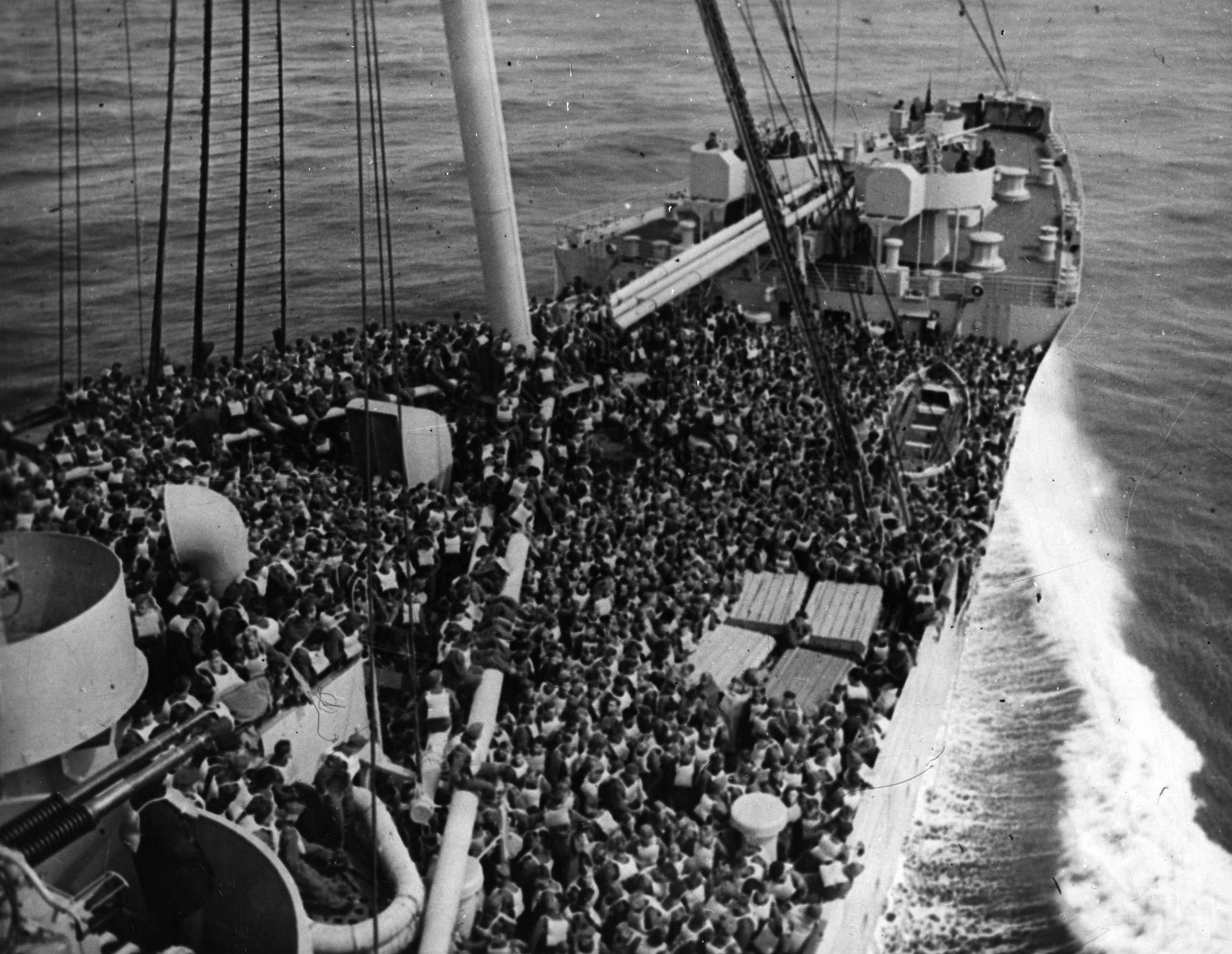 Troops crowd the deck during a lifeboat drill aboard the Queen Mary in December 1944. The luxury liner churns the sea swiftly, her captain and crew wary of the threat of German U-boats. 
