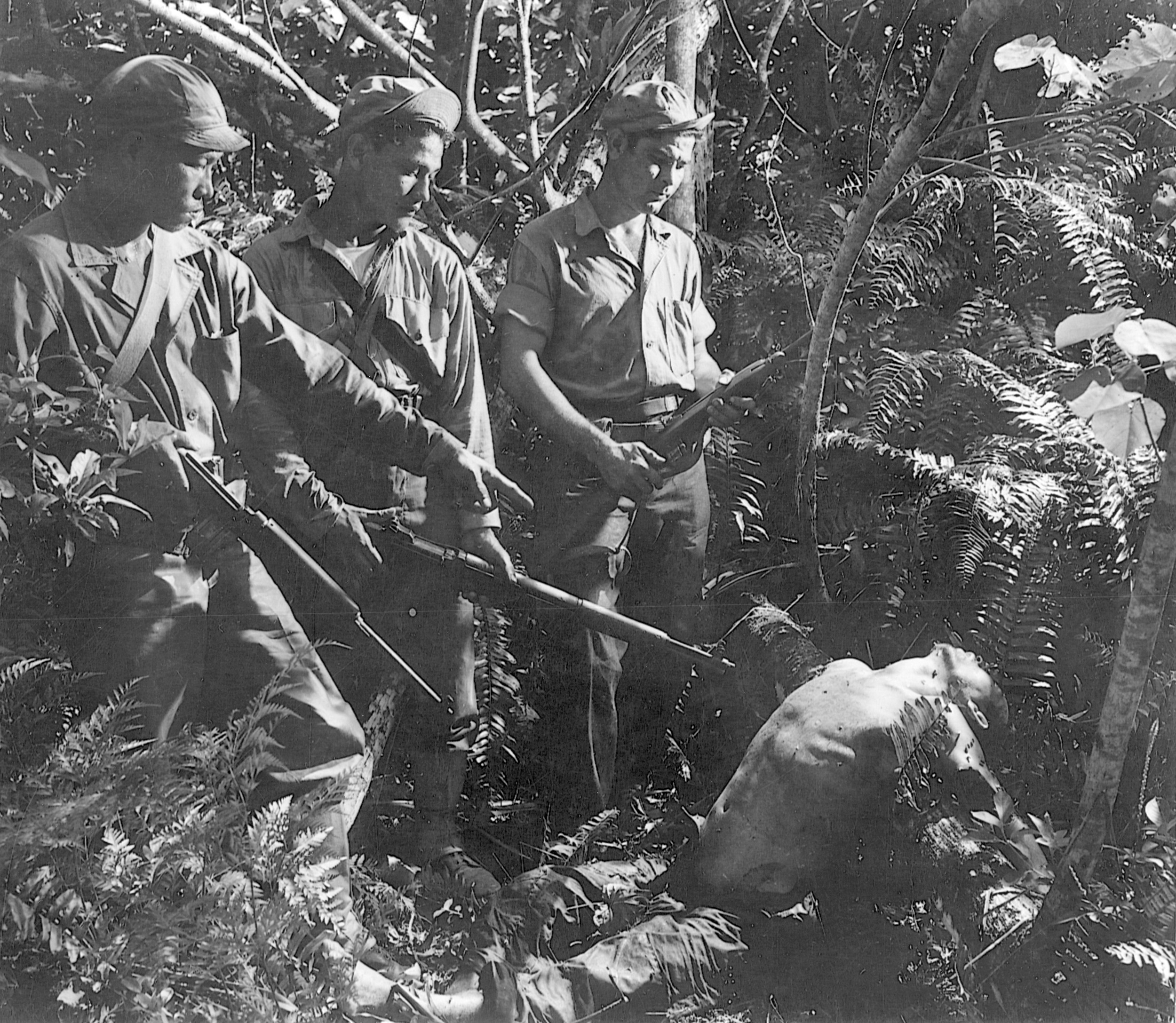 With their guns at the ready, members of a native military patrol stand over the body of a dead Japanese soldier on Guam in the Marianas.