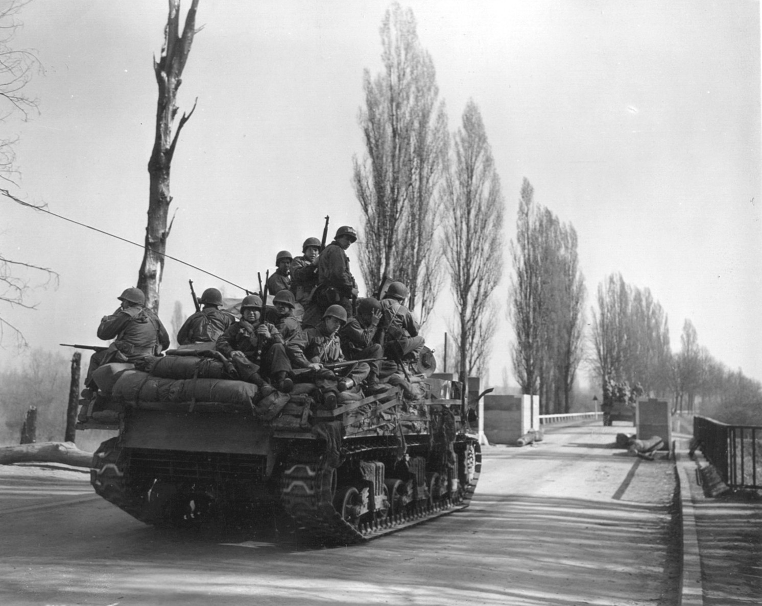 U.S. tanks loaded with infantrymen pass through a final roadblock before crossing the Rhine River.