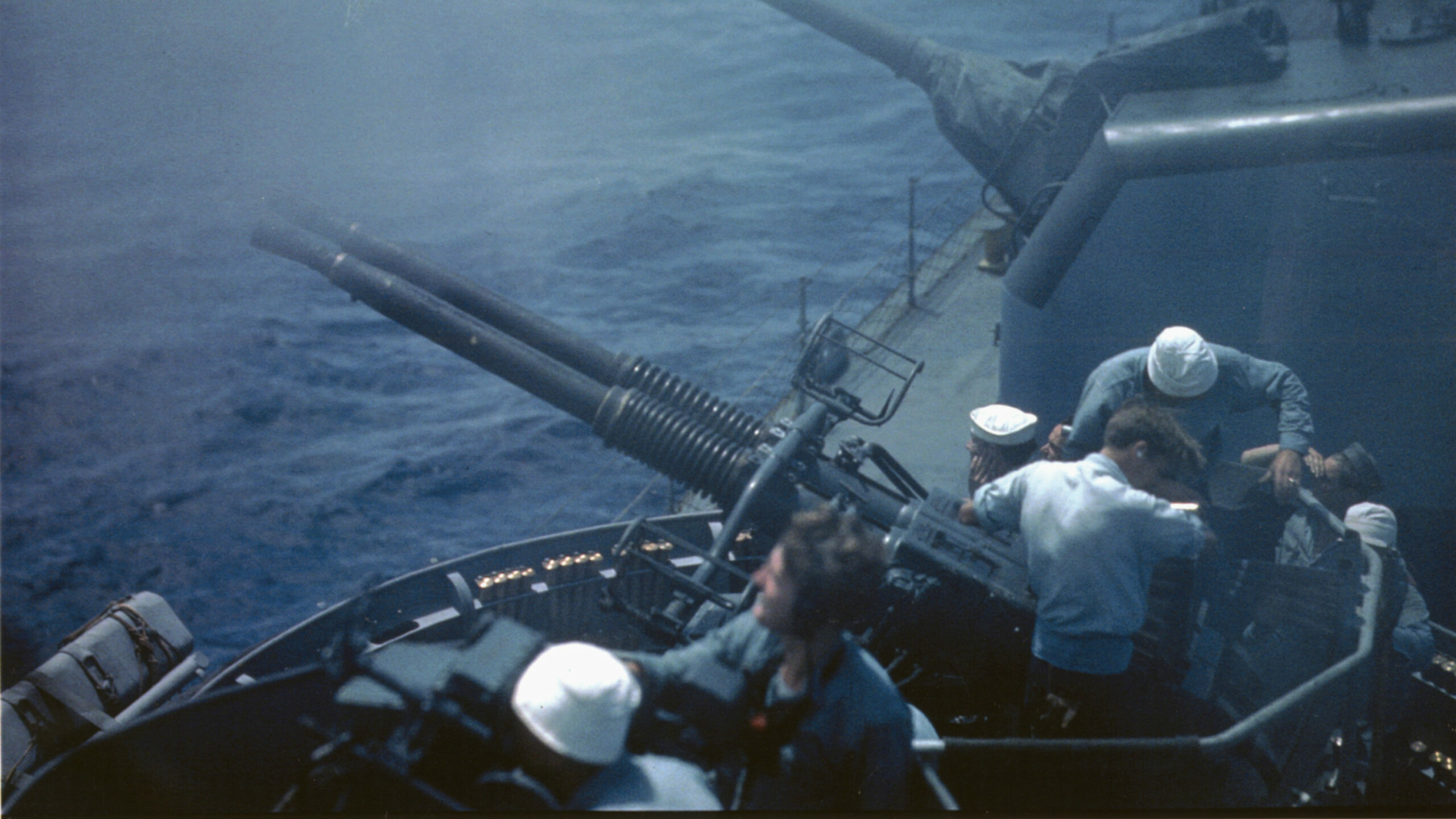 Crewmen service the quad mounted 40mm cannon aboard a U.S. Navy destroyer escort. A 5-inch gun turret is visible in the background.