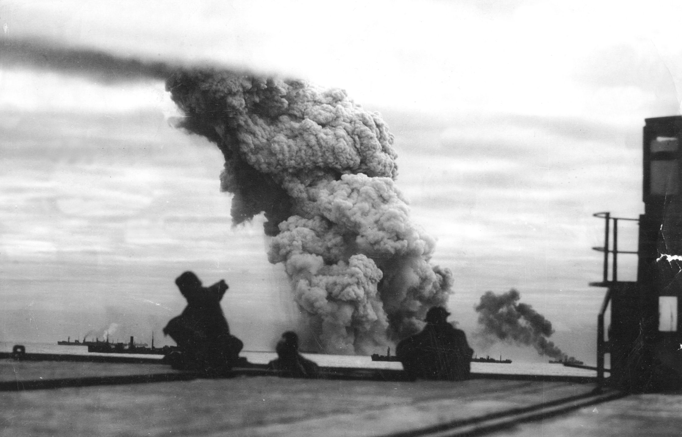 Victims of a German air attack, two Allied merchant ships billow smoke while sailors aboard other vessels look on in October 1942. Despite fearful losses, convoys continued to deliver vital supplies to the Soviet Union.