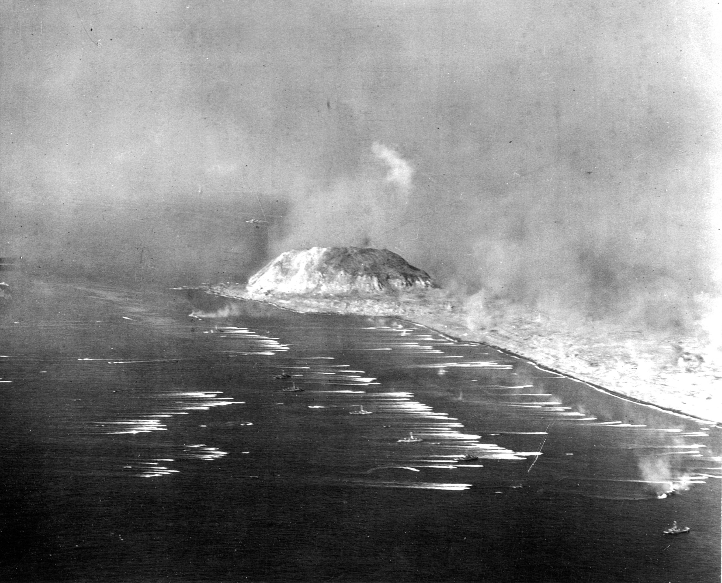 Mount Suribachi, 550 feet high, looms in the background as U.S. Marines assault the beaches of Iwo Jima on February 19, 1945. The wakes of dozens of landing craft are visible in this image.