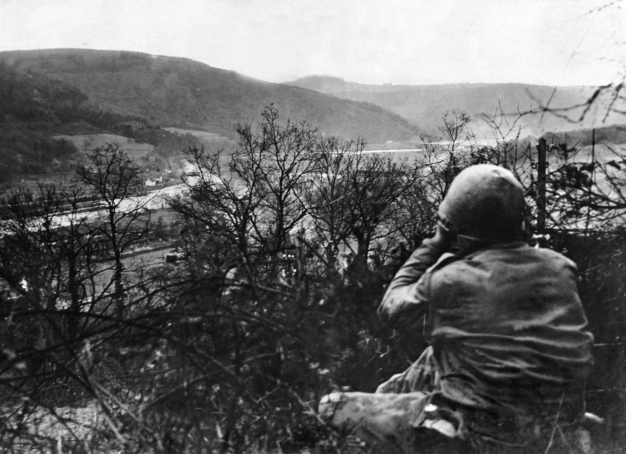 An American soldier surveys the landscape of the Hürtgen Forest near the Roer River through a pair of binoculars. The height of Hill 400 gave its American defenders a panoramic view of the river and the surrounding countryside.