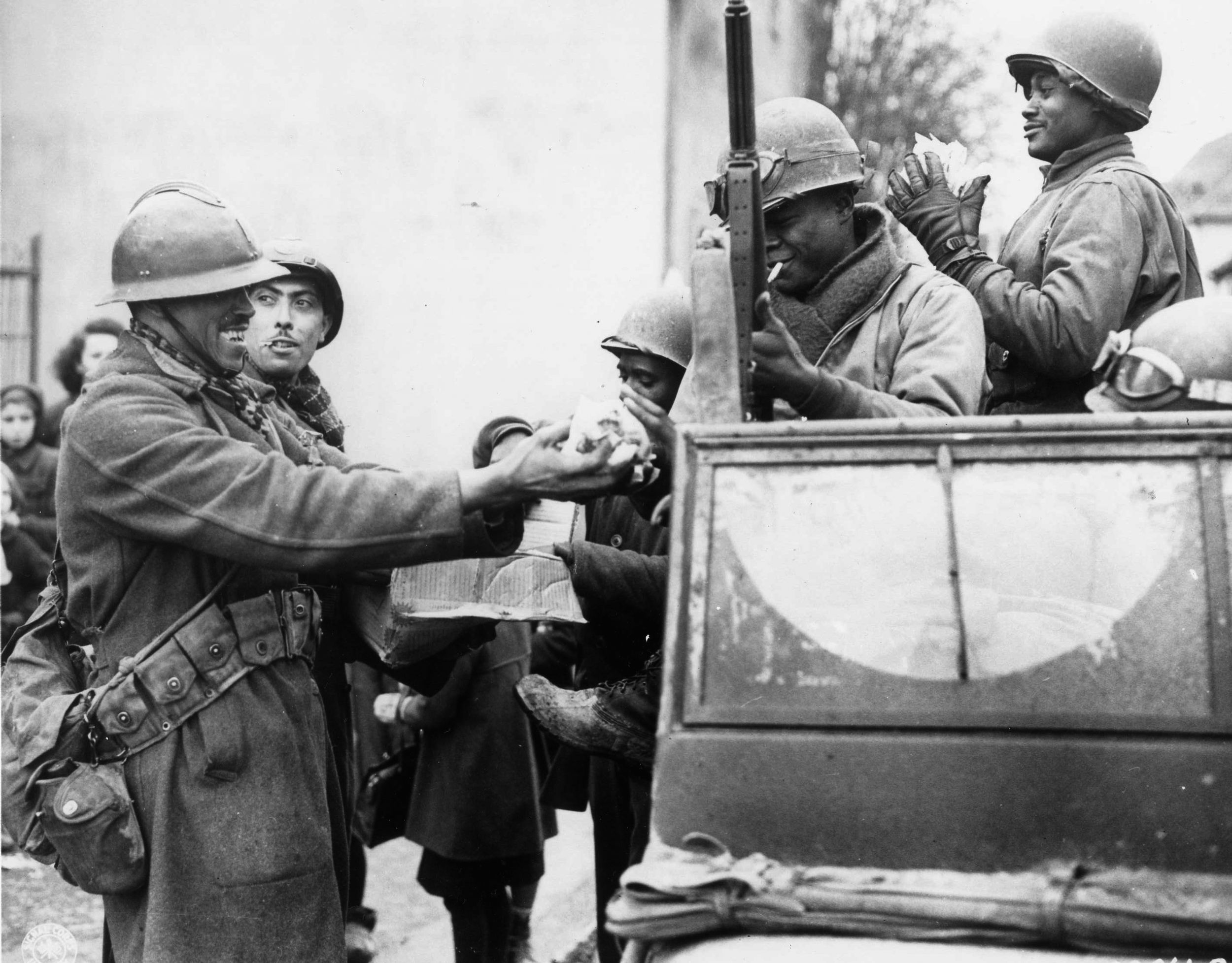 Following the closing of the Colmar Pocket, two smiling French soldiers fill the hands of American troops with candy at Roufflach, France, on February 5, 1945. 