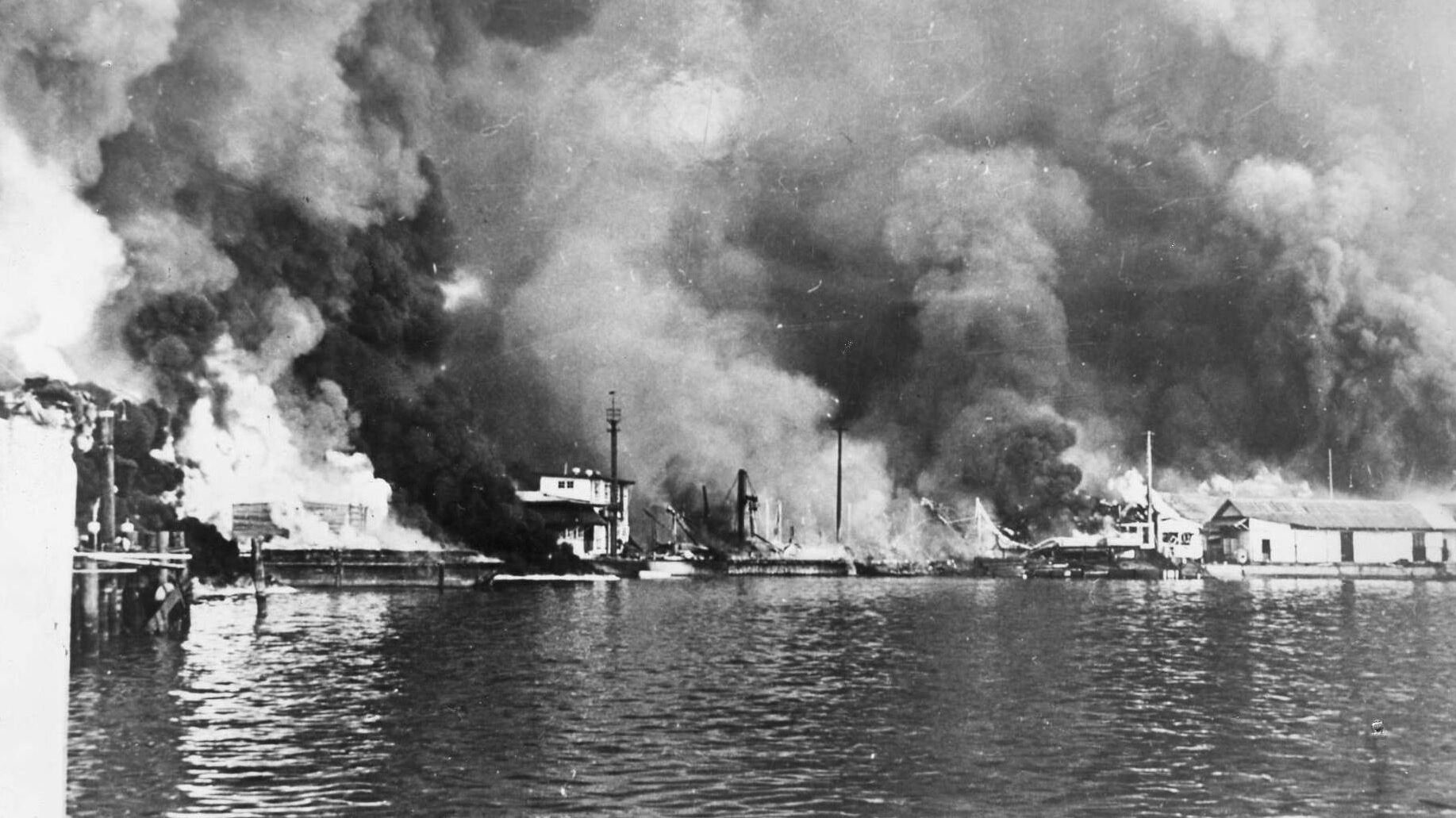 Under attack five days after Pearl Harbor, shore installations and U.S. Navy barges at Cavite in the Philippines burn furiously following a Japanese air raid.