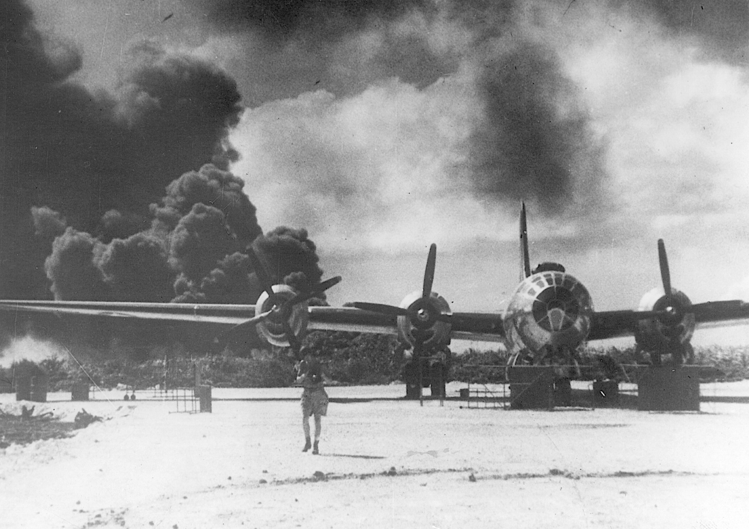 A heavy pall of smoke surrounds a burning oil tank while a parked B-29 sits out of harm’s way following a Japanese air raid on Saipan, December 21, 1944.