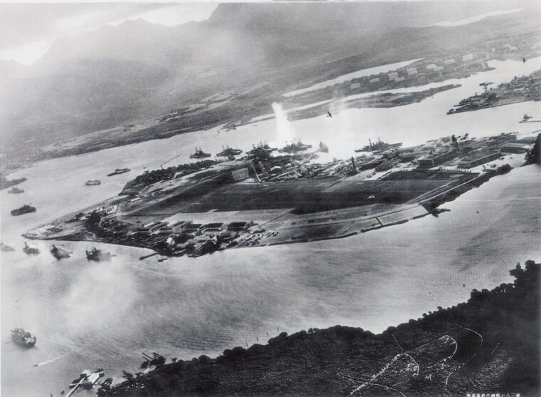 Visible at upper right, a Japanese torpedo bomber banks away from Battleship Row on December 7. A geyser from the impact of a torpedo is clearly visible in the center of the photo; this strike appears to have hit either the battleship West Virginia or Oklahoma.