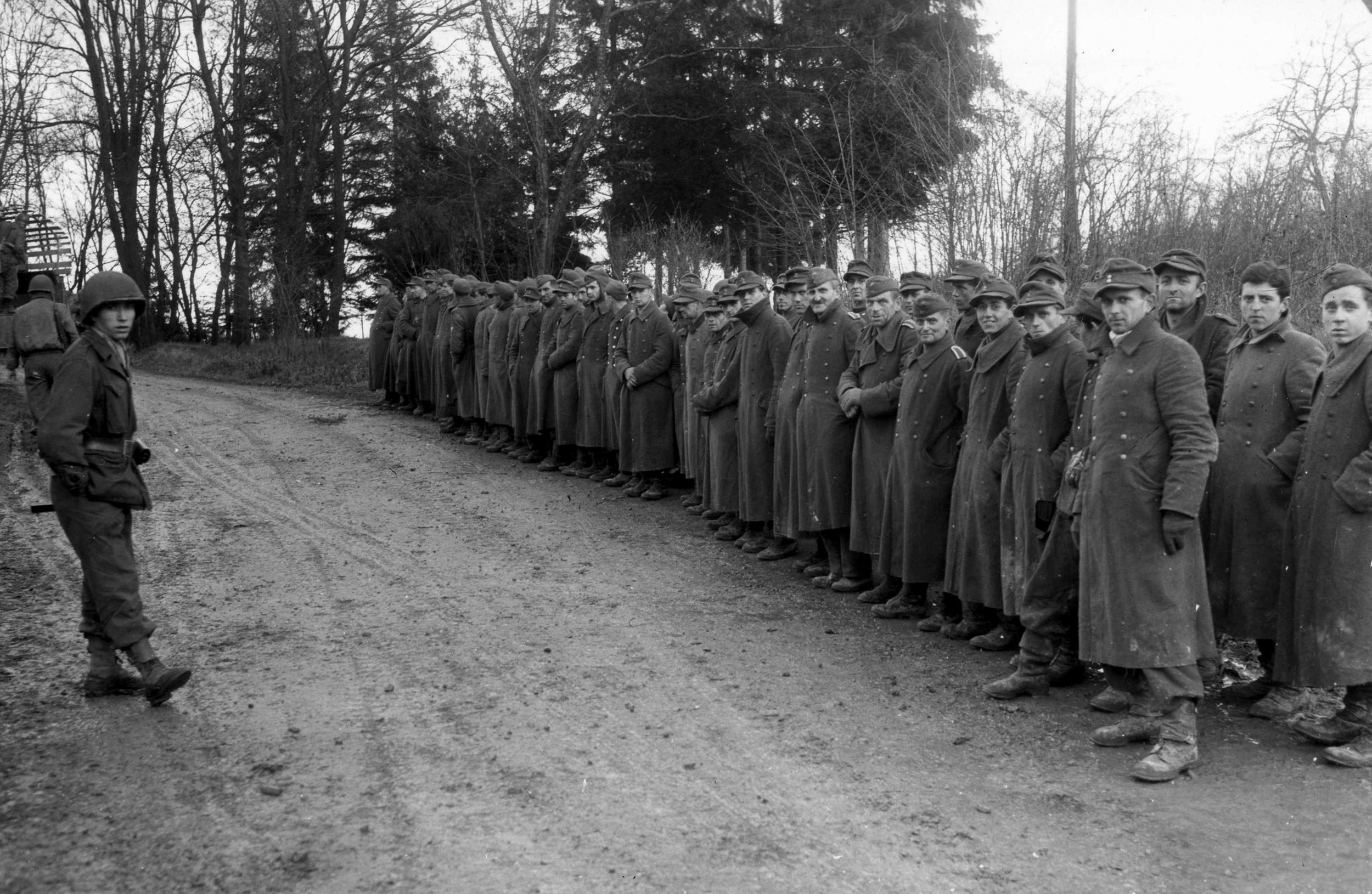 Lined up along a road to await transportation to long-term captivity, German prisoners of war appear fatigued and defeated on December 5, 1944. Eleven days later, the Battle of the Bulge erupted to the north.