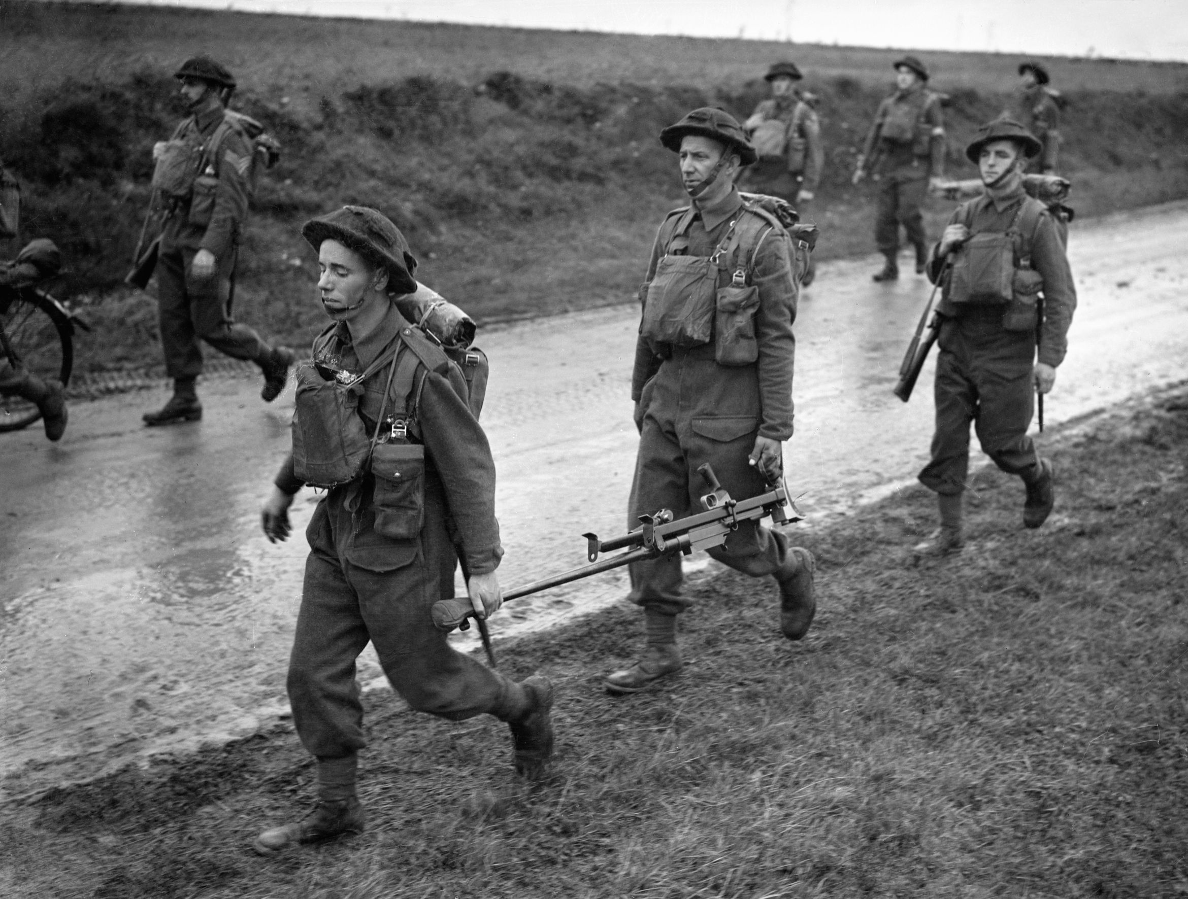Men of the Royal Irish Fusiliers trudge down a road near the French town of Arras in October 1940.  Two of the soldiers, in the foreground, share the burden of a Boys antitank rifle.