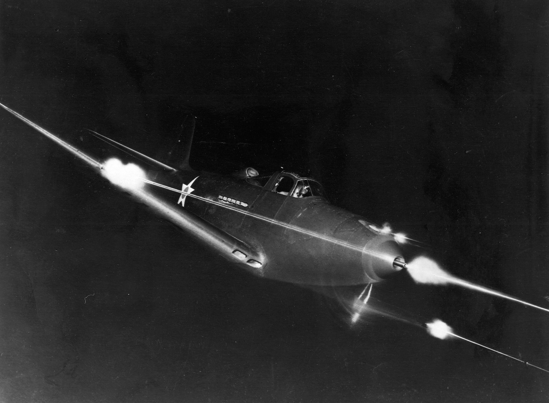 A P-39 bearing U.S. markings lets loose with a barrage of lead from its wing and nose mounted cannons. The P-39 was heavily armed and could be a formidable foe to targets both on the ground and in the air.