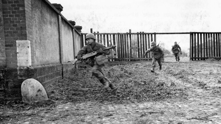 An American machine gunner sprints for cover while carrying his Browning .30-caliber machine gun as an ammunition carrier follows, his rifle slung across his back. This photo was taken in the French arrondissement of Sarreguemines at the height of the fighting in the Colmar Pocket during early February 1945.