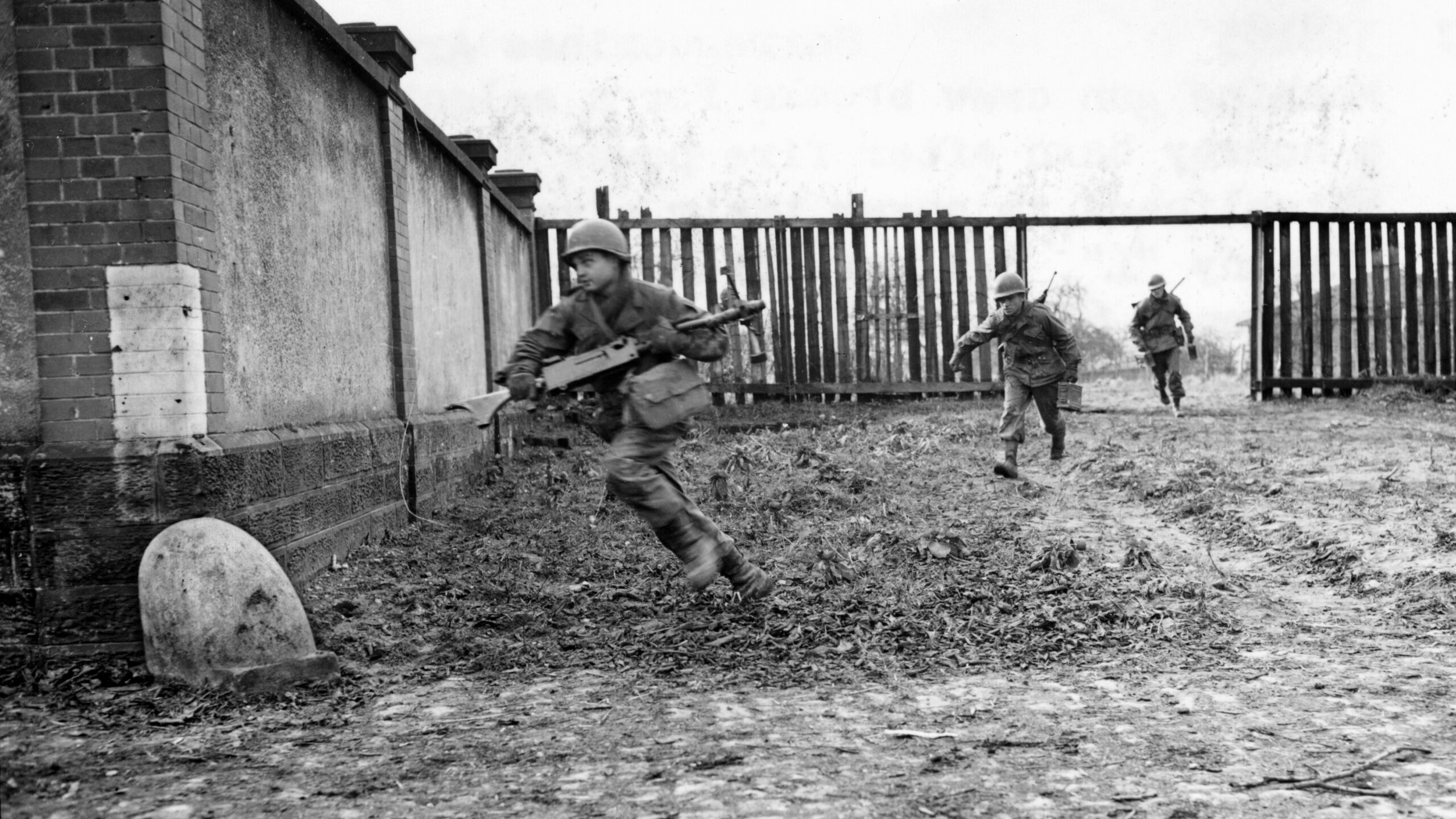 An American machine gunner sprints for cover while carrying his Browning .30-caliber machine gun as an ammunition carrier follows, his rifle slung across his back. This photo was taken in the French arrondissement of Sarreguemines at the height of the fighting in the Colmar Pocket during early February 1945.