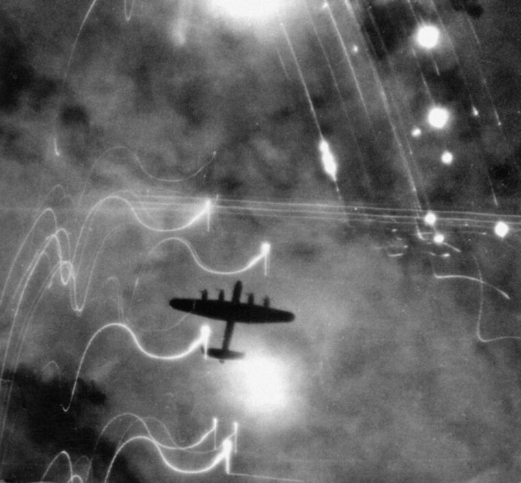 Looking down on a British Lancaster bomber over Hamburg. Fires on the ground and the white streaks of anti-aircraft munitions are clearly visible.