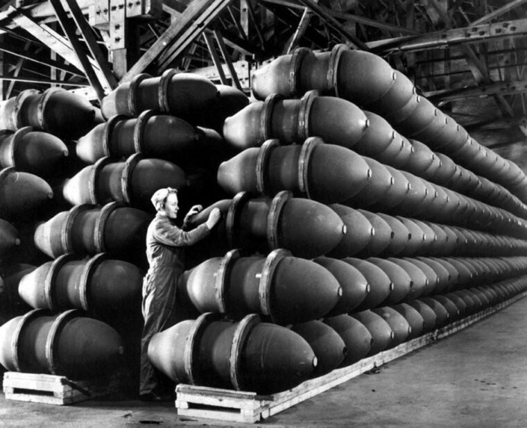 A female worker in an ordnance plant poses with stacks of 500-pound bombs.