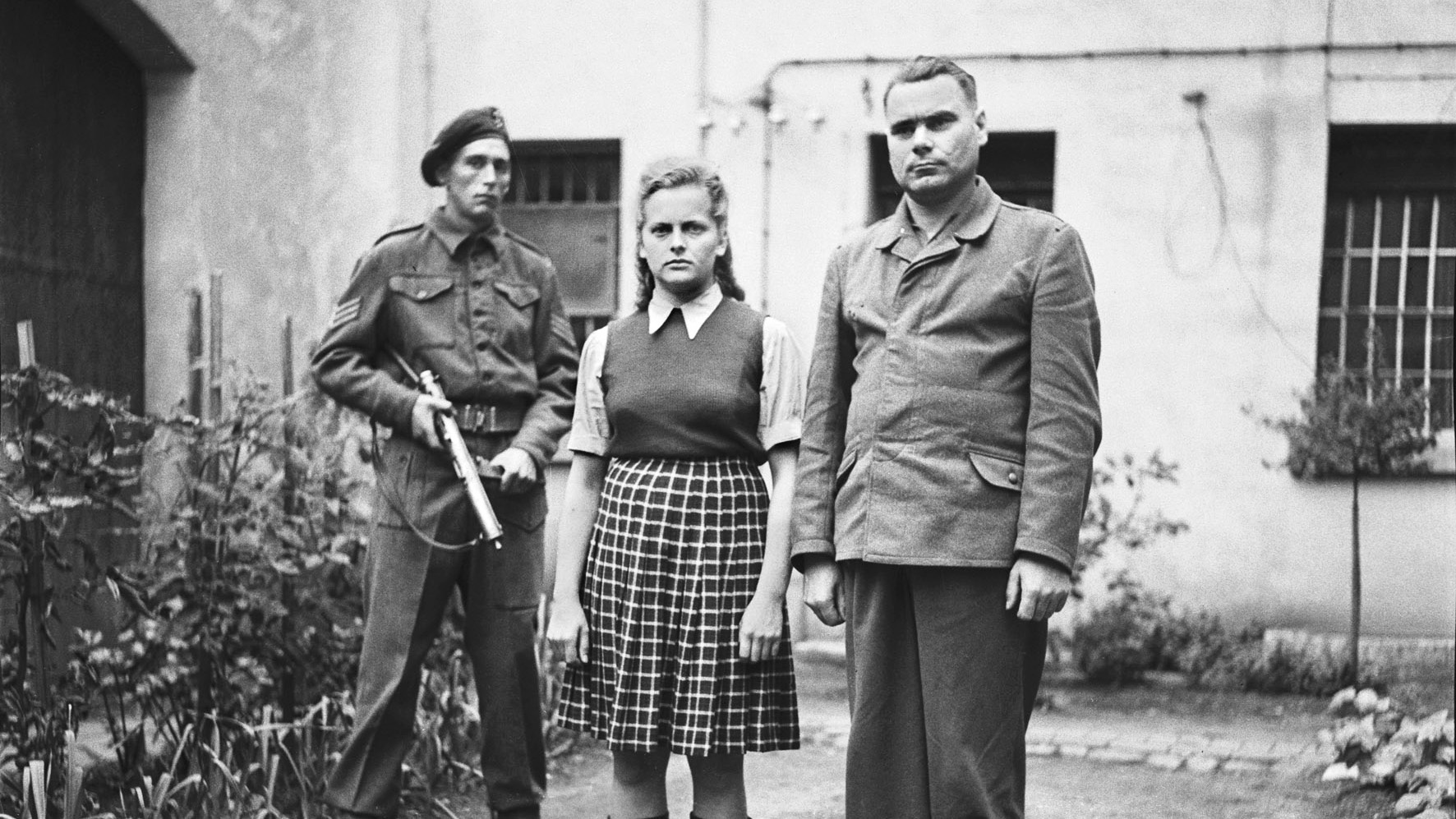 In jackboots and civilian clothes, Irma Grese (along with Bergen-Belsen commandant Josef Kramer, right) stands in the courtyard of the prison at Celle during their war-crimes trial, June 1945.