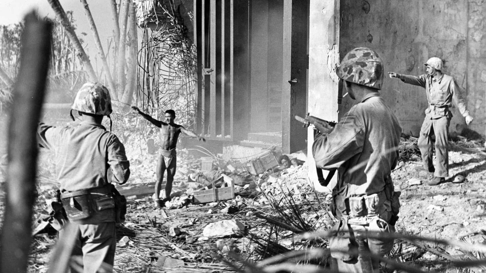 Weary of fighting, a Japanese soldier raises his hands in surrender at Roi-Namur as a companion begins climbing out of a hole near the center of this photograph. These are two of only a handful of Japanese troops that survived the fighting on Roi-Namur, choosing surrender rather than suicide. A wary Marine covers the prisoner with his rifle, taking no chances.