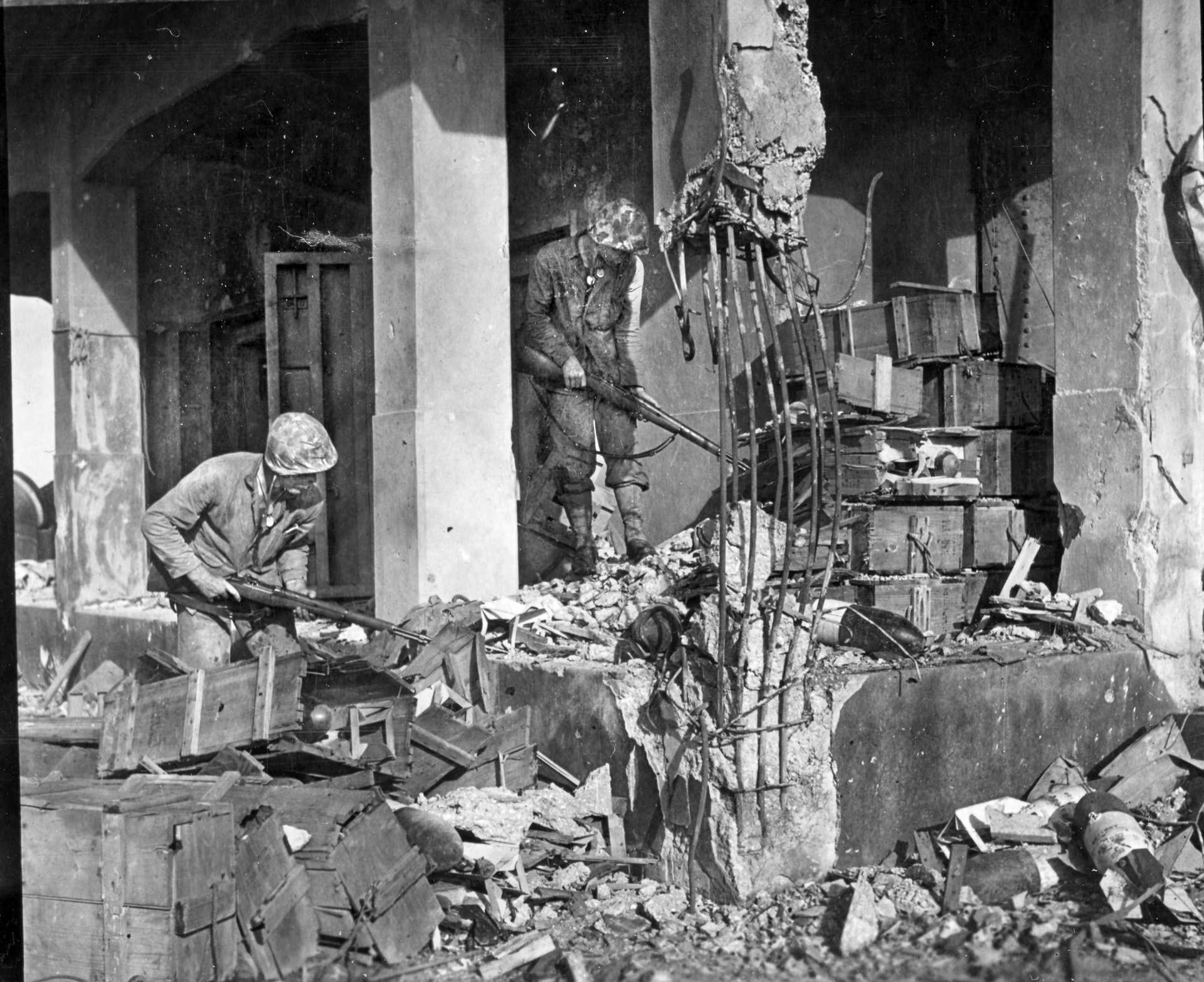 Cautious with every step, these Marines pick their way through the ruins of a building previously used by the Japanese on Roi-Namur to store ammunition.