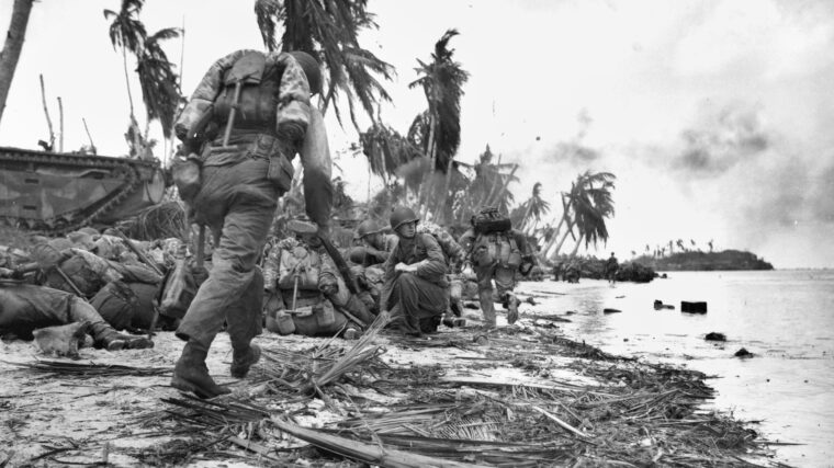 Marines pause on one of the invasion beaches on Guam in July 1944. An amphibious tracked vehicle is seen at left, while soldiers take up positions and prepare to advance inland.