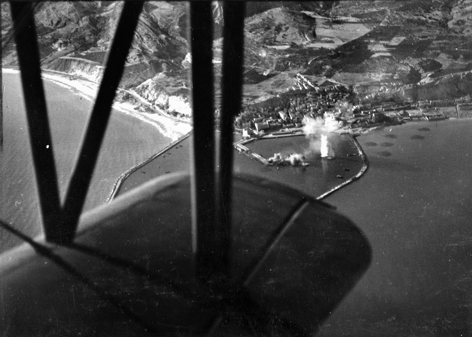 An aerial view from a Curtiss Seagull reveals the accuracy of shells fired from the cruiser USS Philadelphia during the Sicily landings. The target of Philadelphia’s shells is an enemy railway battery located on a jetty at Port Empedocle.