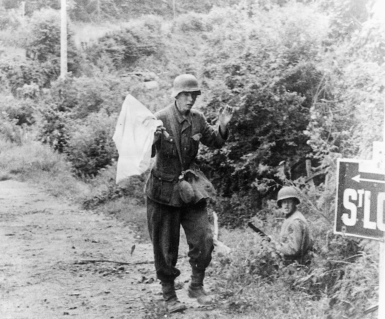 With an American soldier covering his movement, a German soldier surrenders to U.S. forces outside St. Lô.