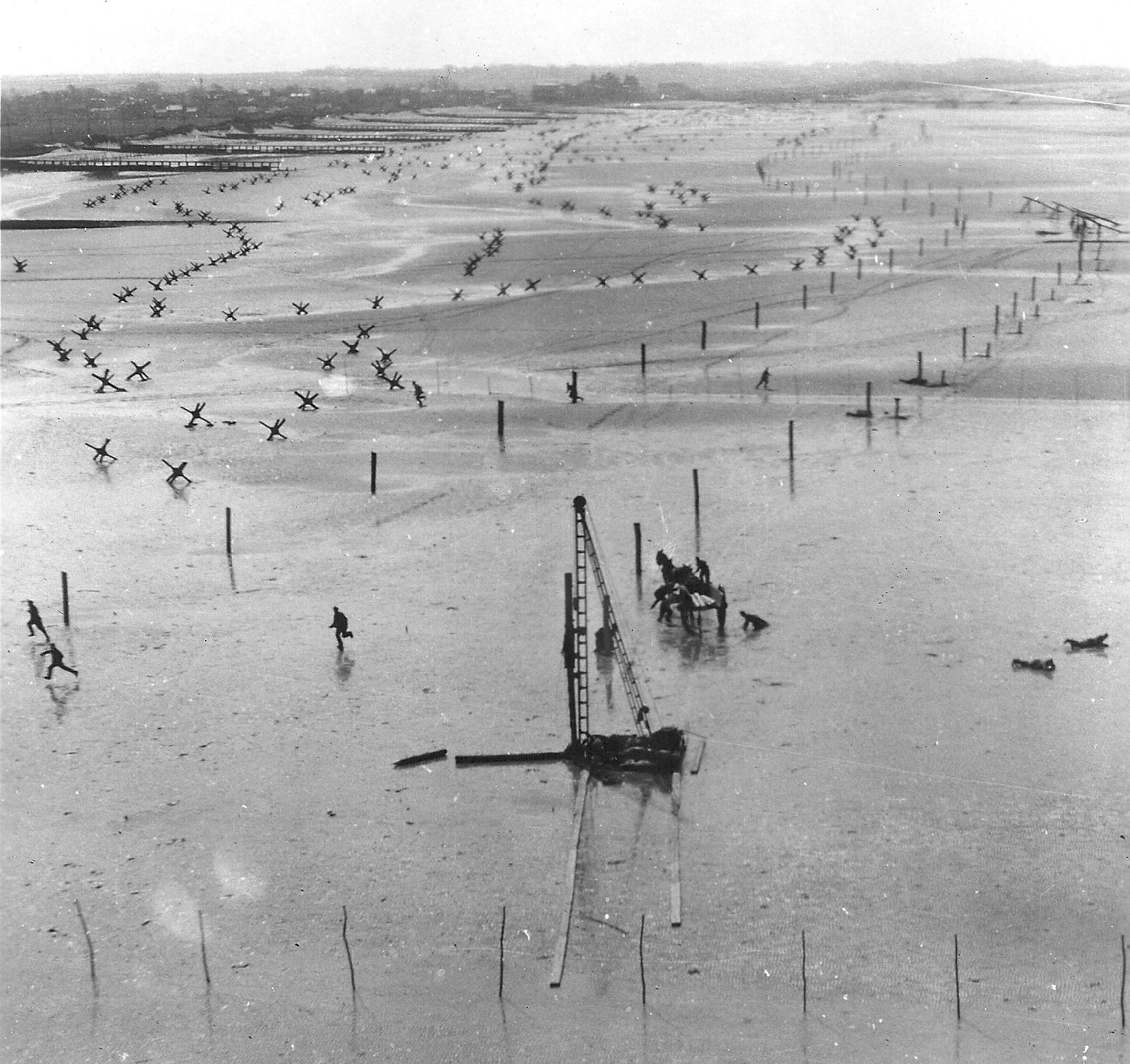 A camera plane recorded this low-angle scene of German troops installing obstacles along Normandy’s Omaha Beach and running for cover shortly before the Allied invasion. (photo by U.S. Army Air Forces)